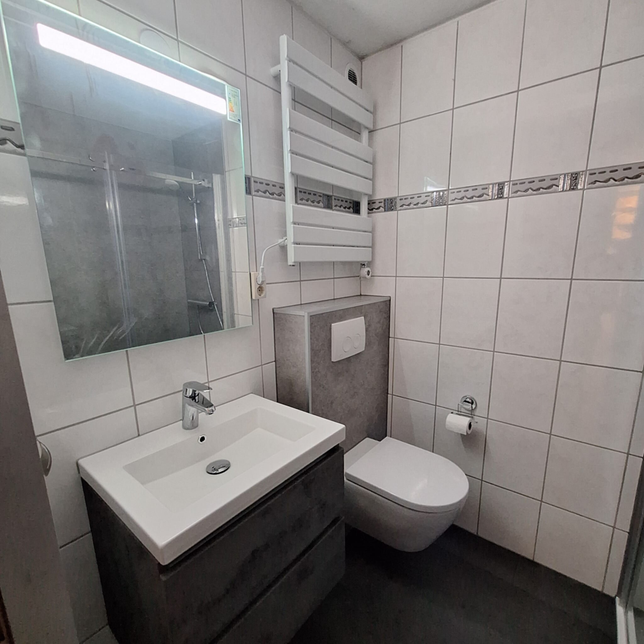 Moderne badkamer met witte en grijze tegels, toilet, wastafel en douche