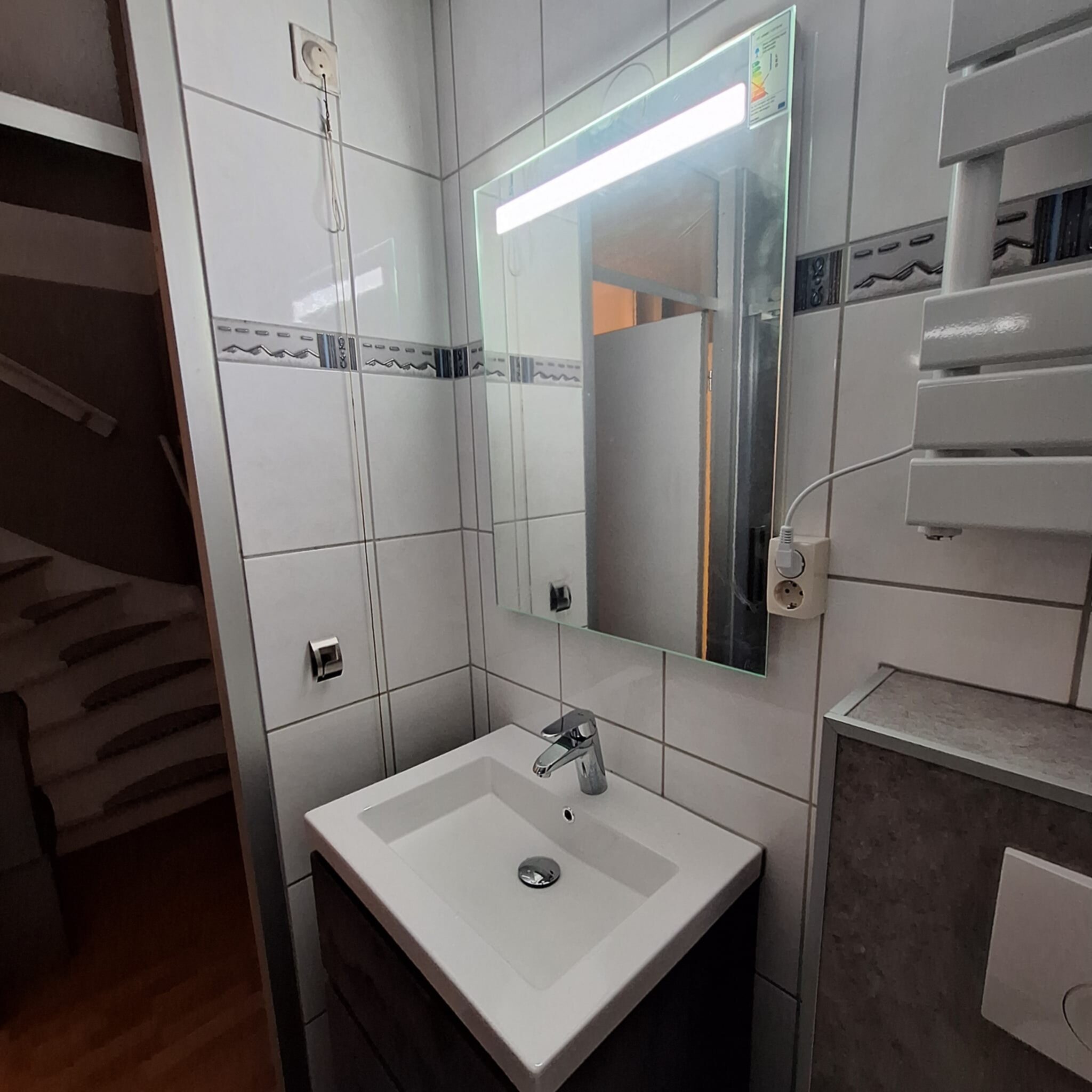 Wit betegelde badkamer met wastafel en spiegel