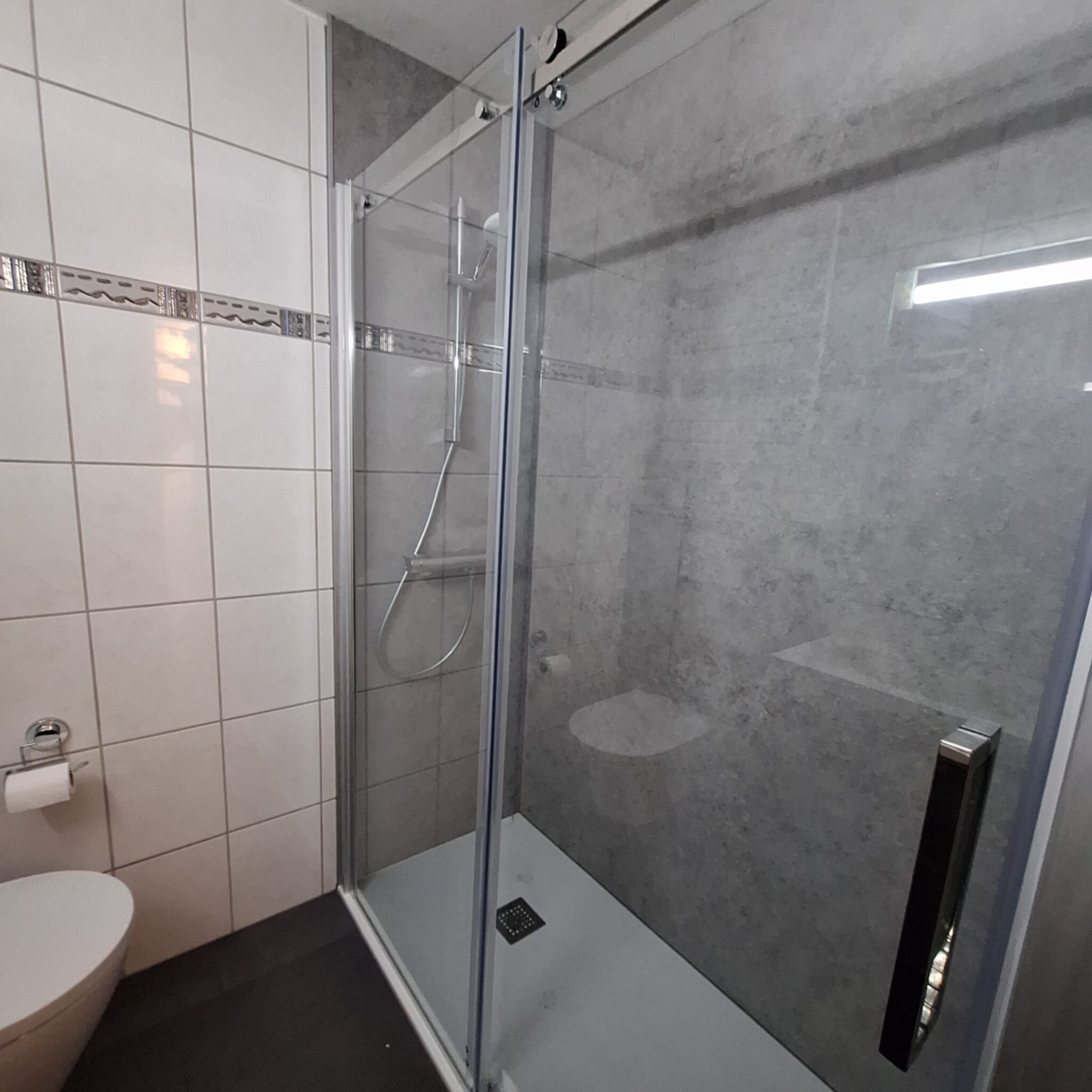 Douchecabine met glazen deur en witte toilet in moderne badkamer