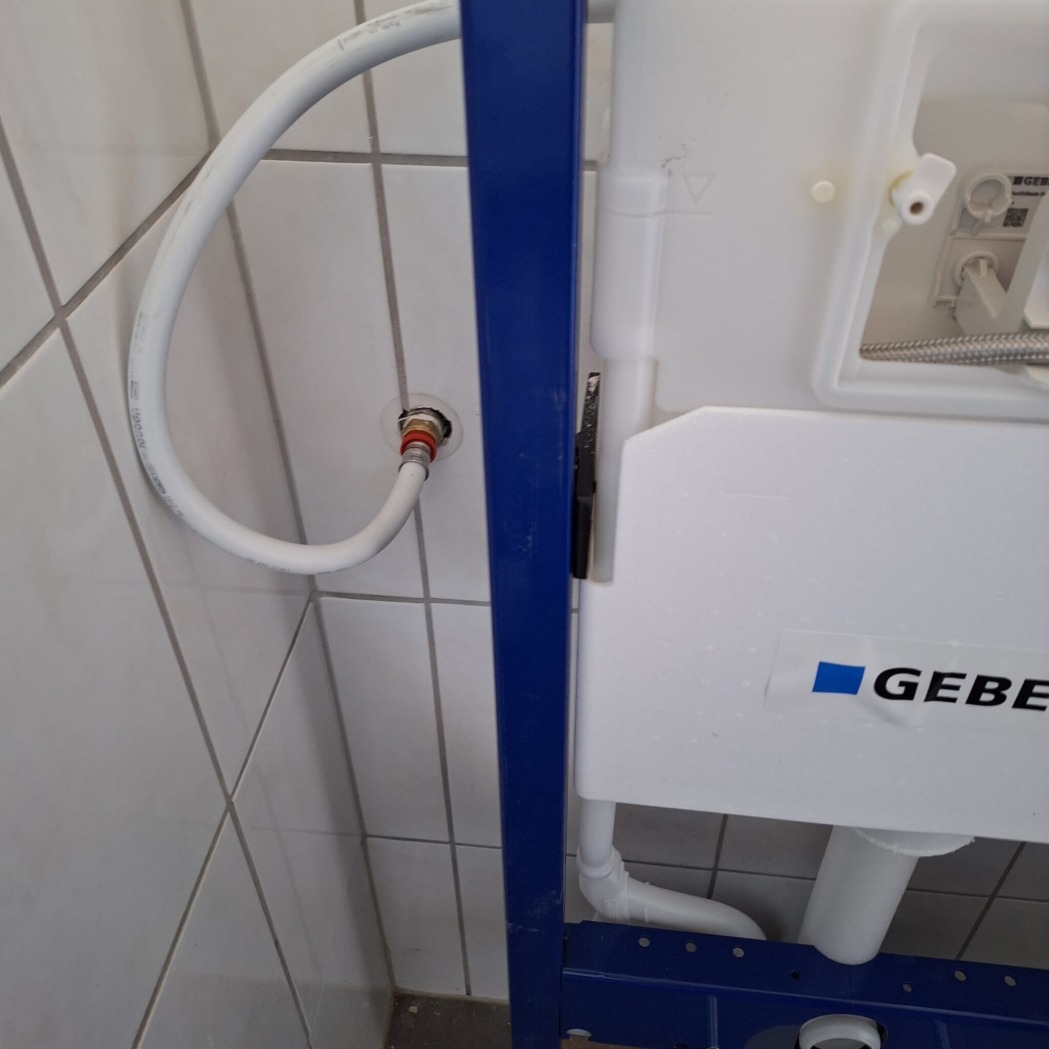Wit betegelde badkamer met blauwe metalen steun en witte waterleidingen