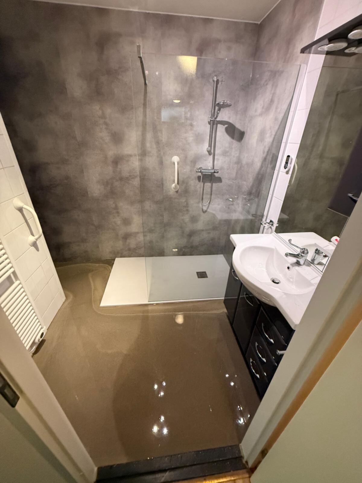 Badkamer met grijs betegelde douche en bruine vloer