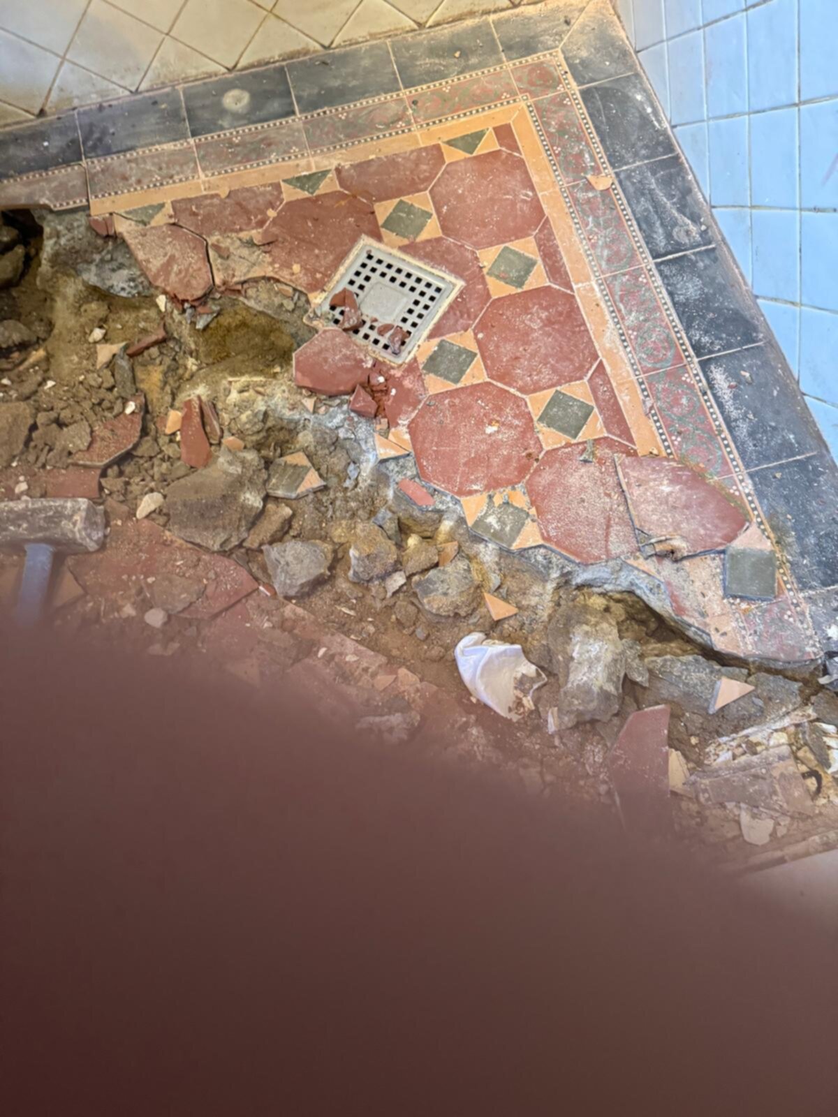 Verbroken tegelvloer met rode en groene tegels in badkamer tijdens renovatie