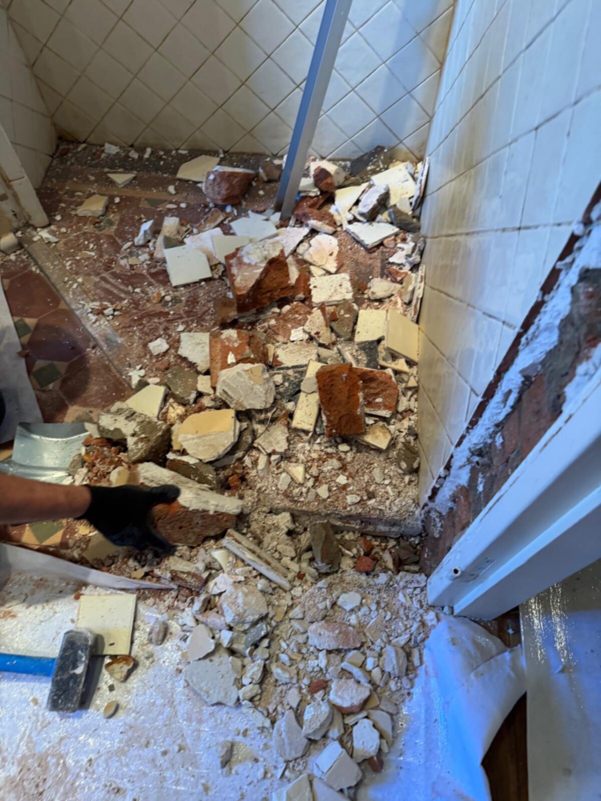 Sloop badkamer met kapotte tegels en puin op de grond