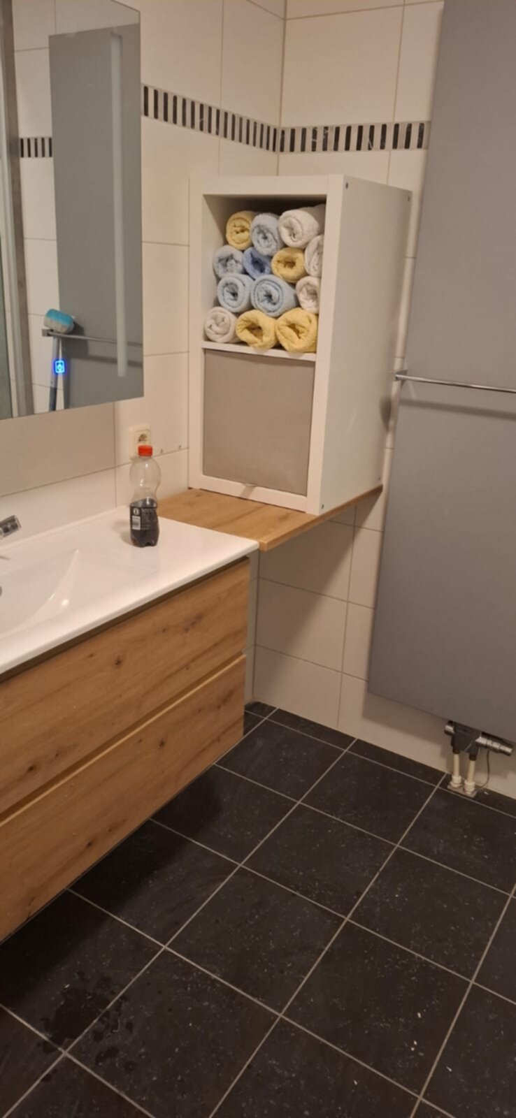 Wit en houten badkamer met donkere tegelvloer en opgerolde handdoeken