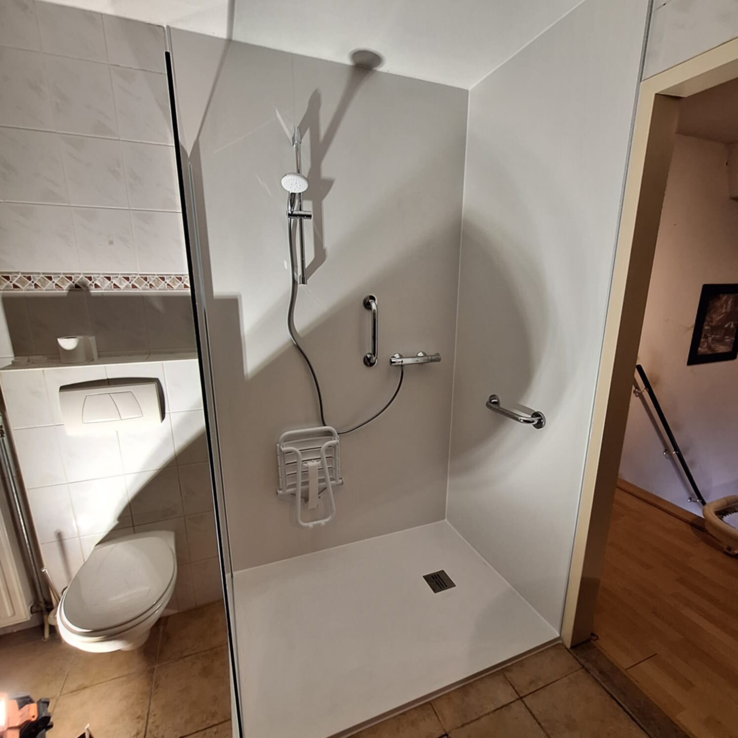 Douchecabine met witte muren en tegelvloer, toilet en douchekop