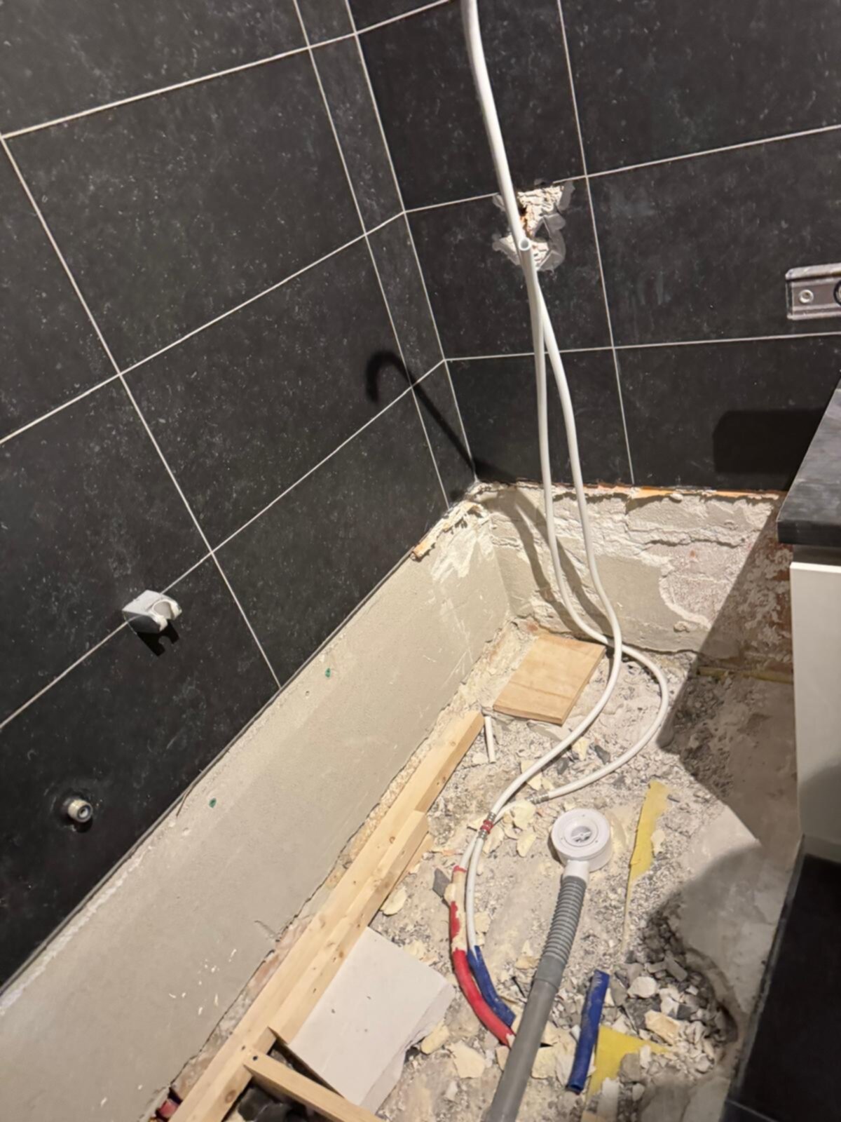 Sleuf in badkamer vloer met ontbrekende tegels en zichtbare leidingen