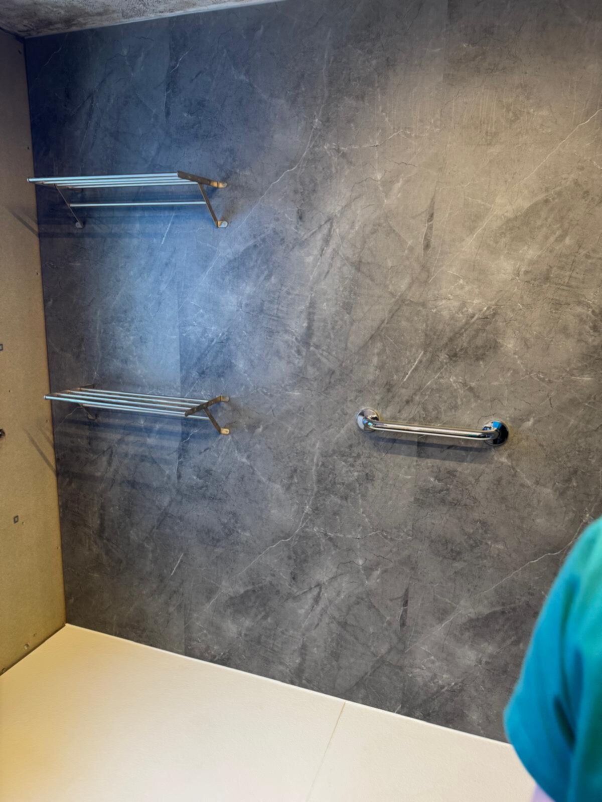 Grijze betegelde badkamerwand met twee metalen rekjes en een handgreep