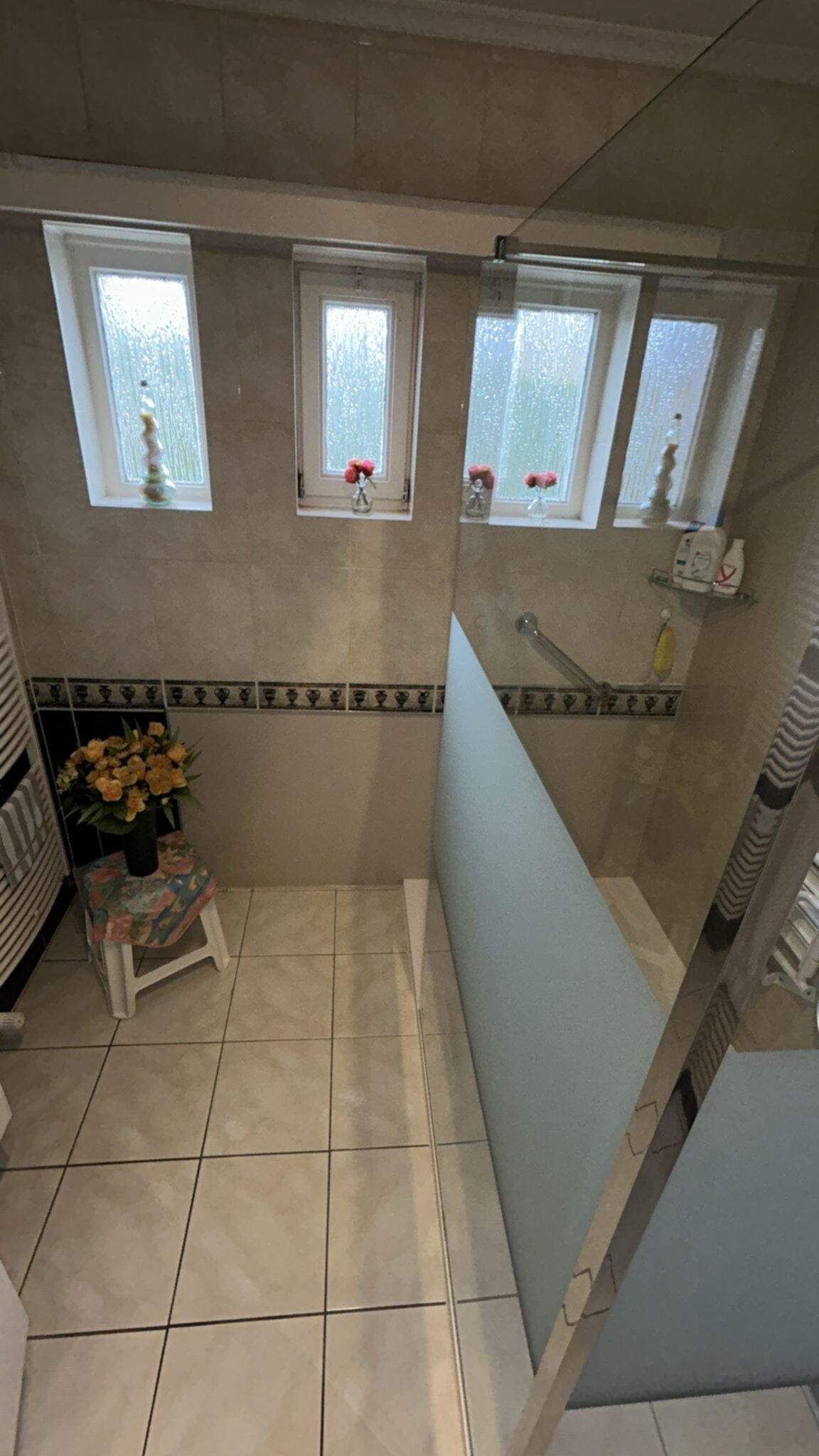 Douche ruimte met beige tegels, glaswand en ramen met rozen