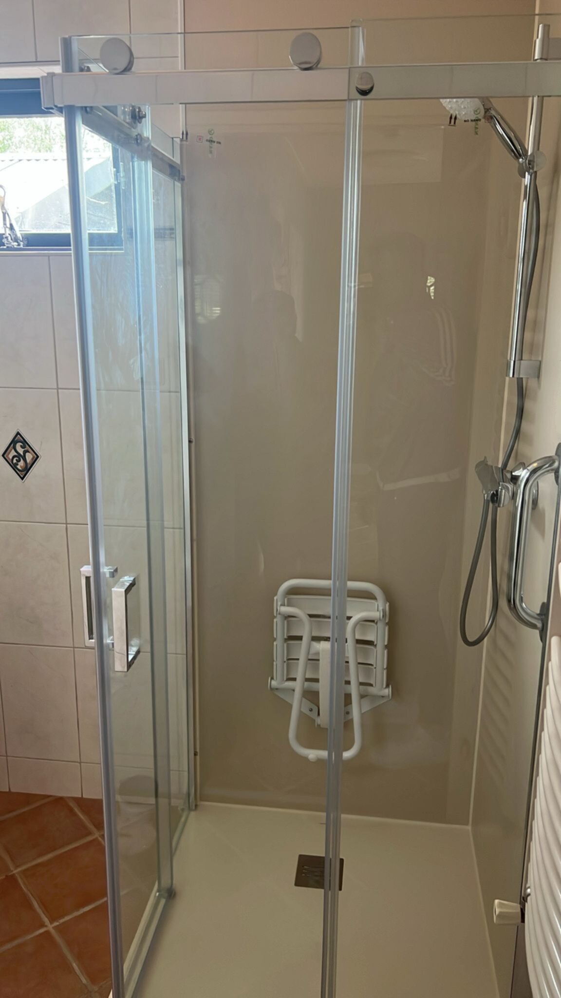 Douchecabine met glazen deur en wand, witte tegel en betegelde vloer