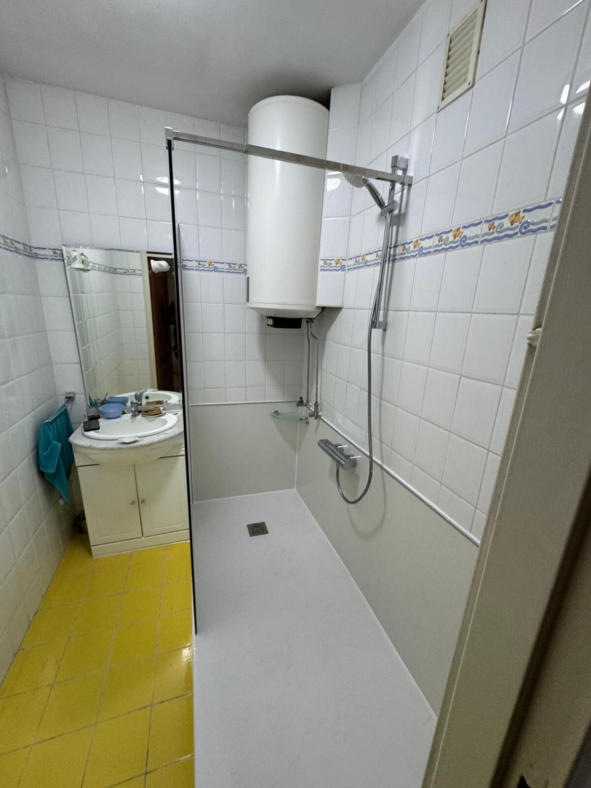 Badkamer met witte tegels en gele vloer, douche en wasbak