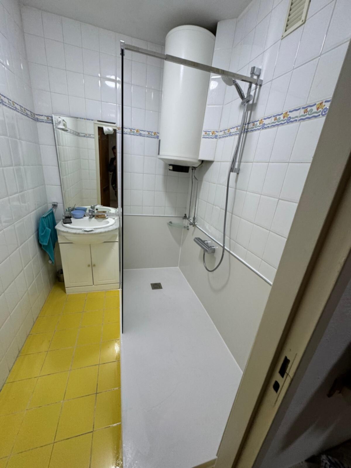 Badkamer met witte tegelwanden, gele vloer en douche