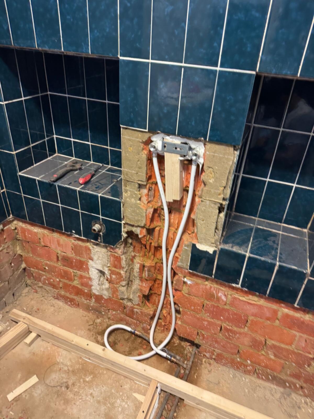 Badkamer renovatie in uitvoering met blootgelegde leidingen en opengebroken tegelwand