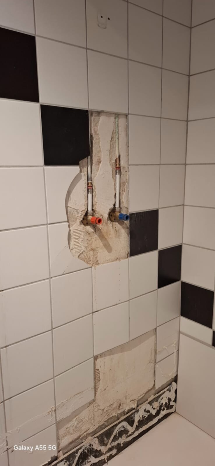 Grote witte en zwarte betegelde wand met openingen voor waterleidingen