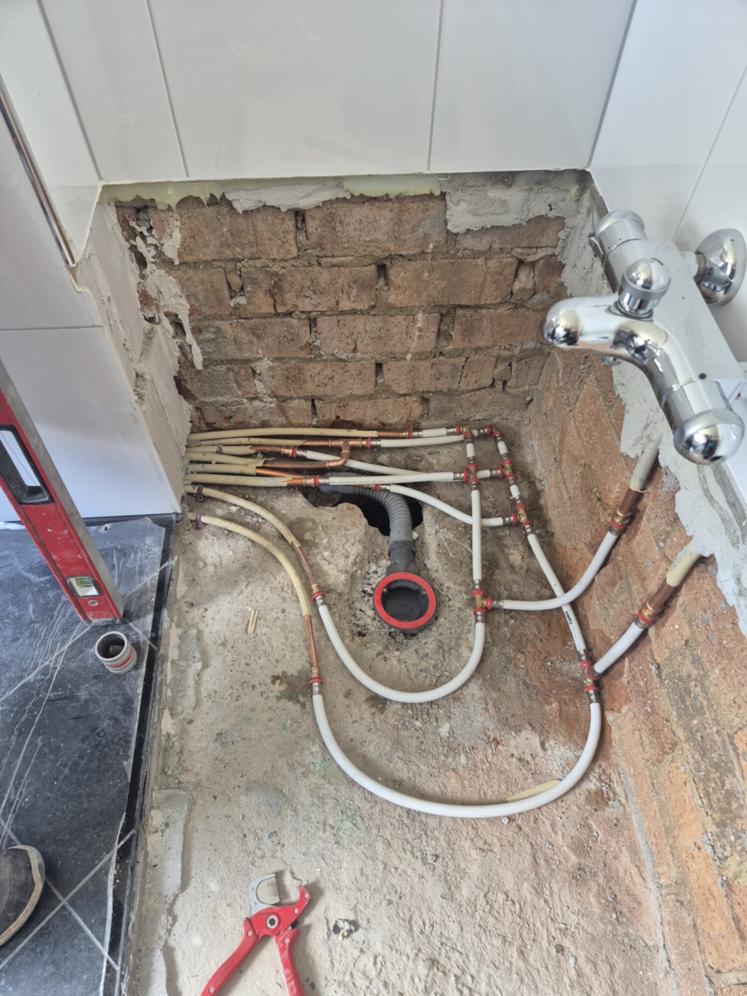 Badkamer renovatie, zicht op de kale bakstenen muur en de leidingen op de grond