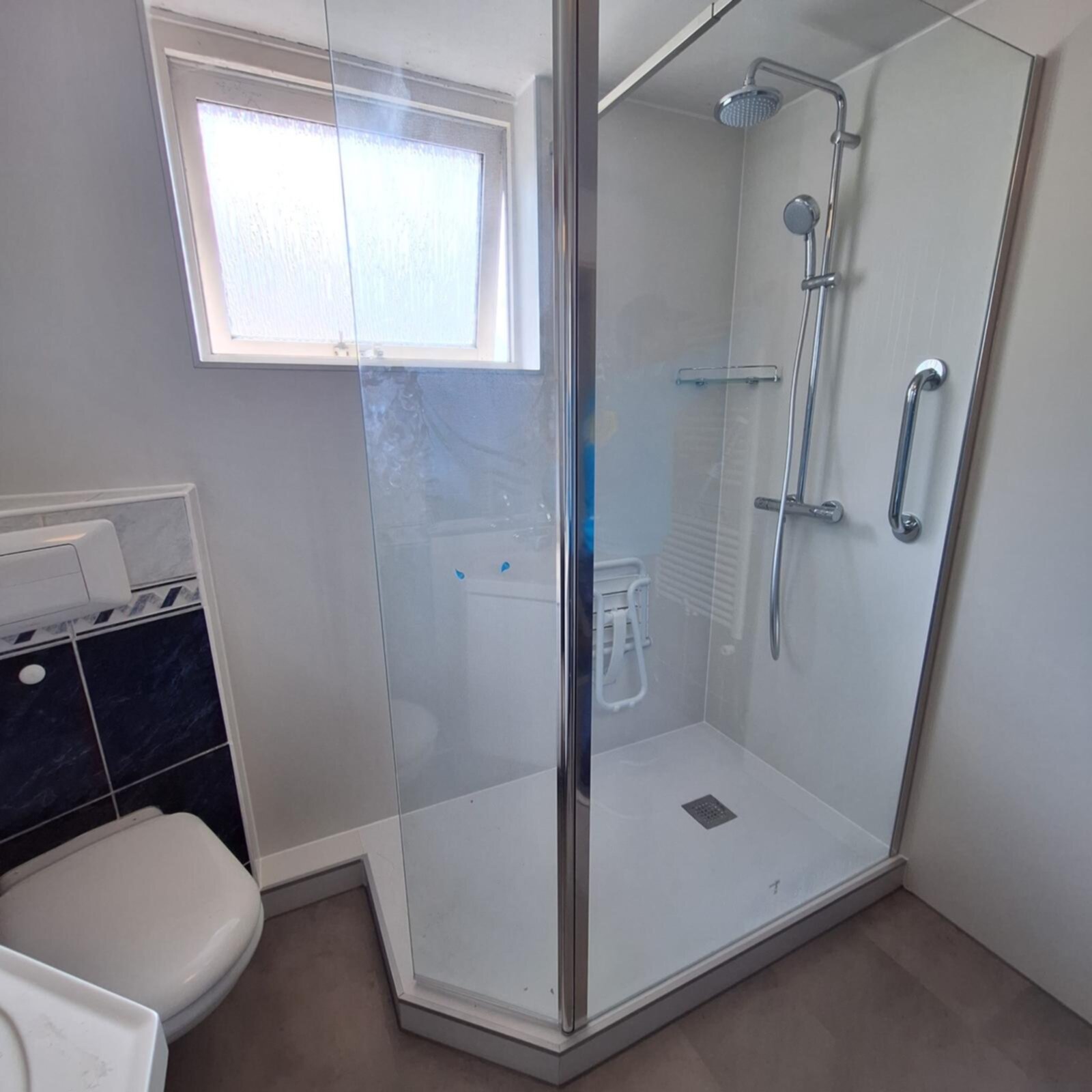 Douchecabine met glazen wand en deur, witte en blauwe tegelwerk, toilet en grijs interieur