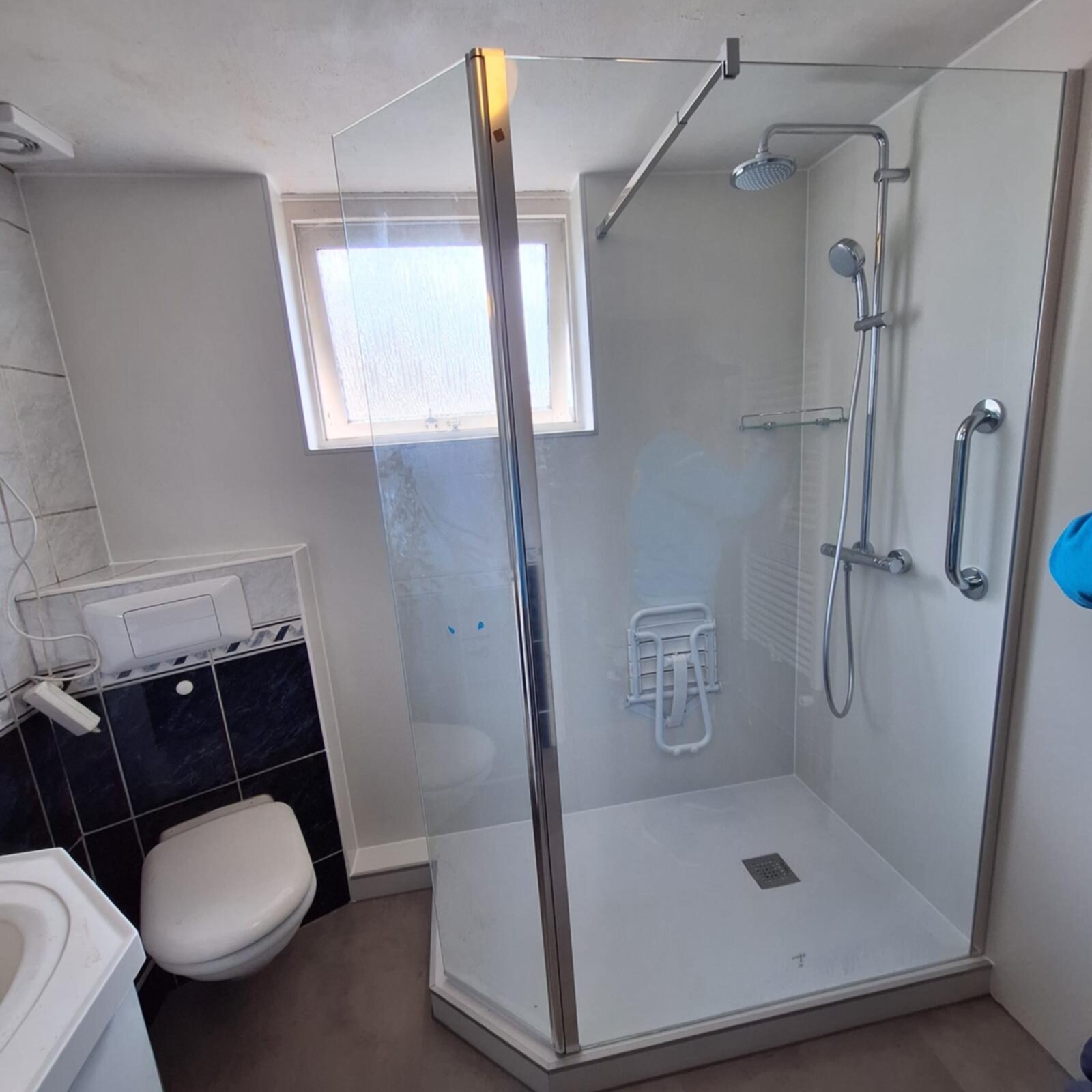 Douchecabine met glazen deur en zilveren kraan, toilet en betegelde wand