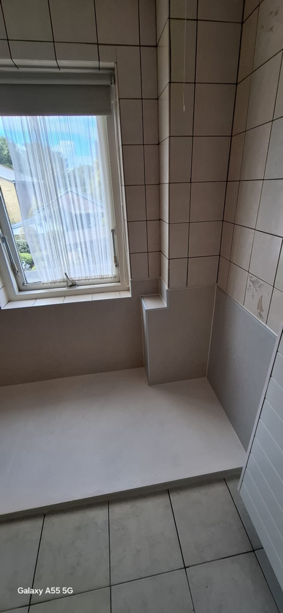 Badkamer met betegelde muren en vloer, raam met gordijn, voorbereid voor douche