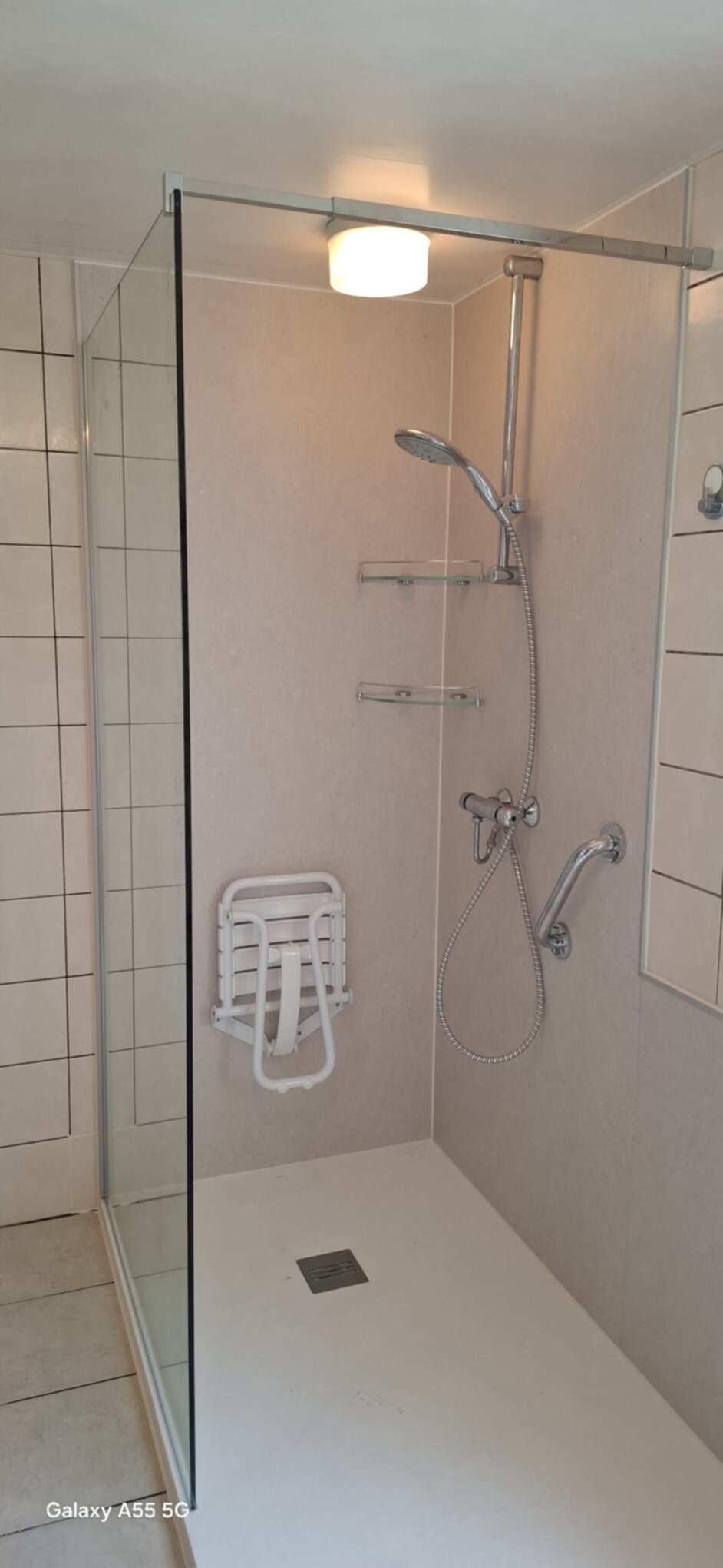 Douchecabine met glazen wand, witte tegelvloer en beige wanden, toegankelijk
