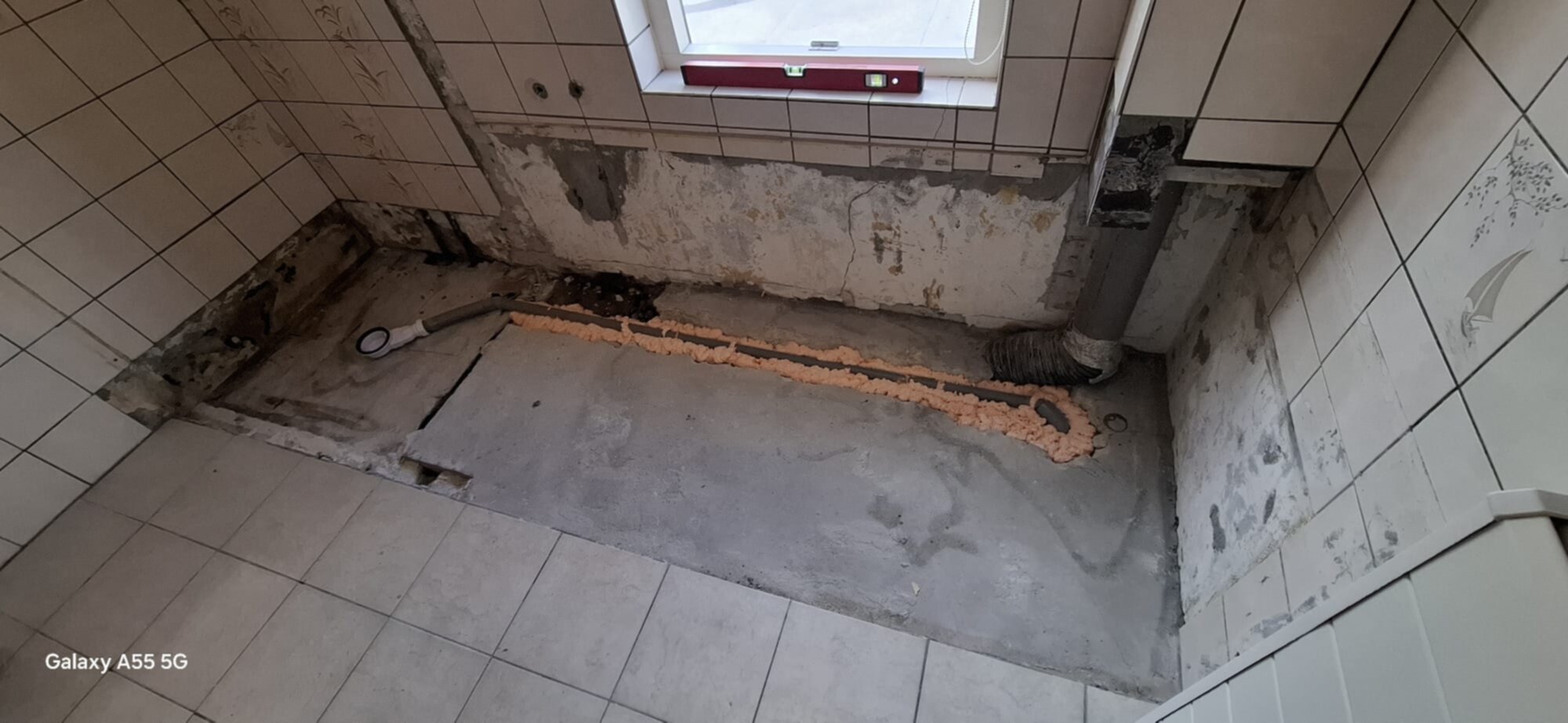 Slecht onderhouden badkamer vloer met beschadigde betegeling en zichtbare leidingen