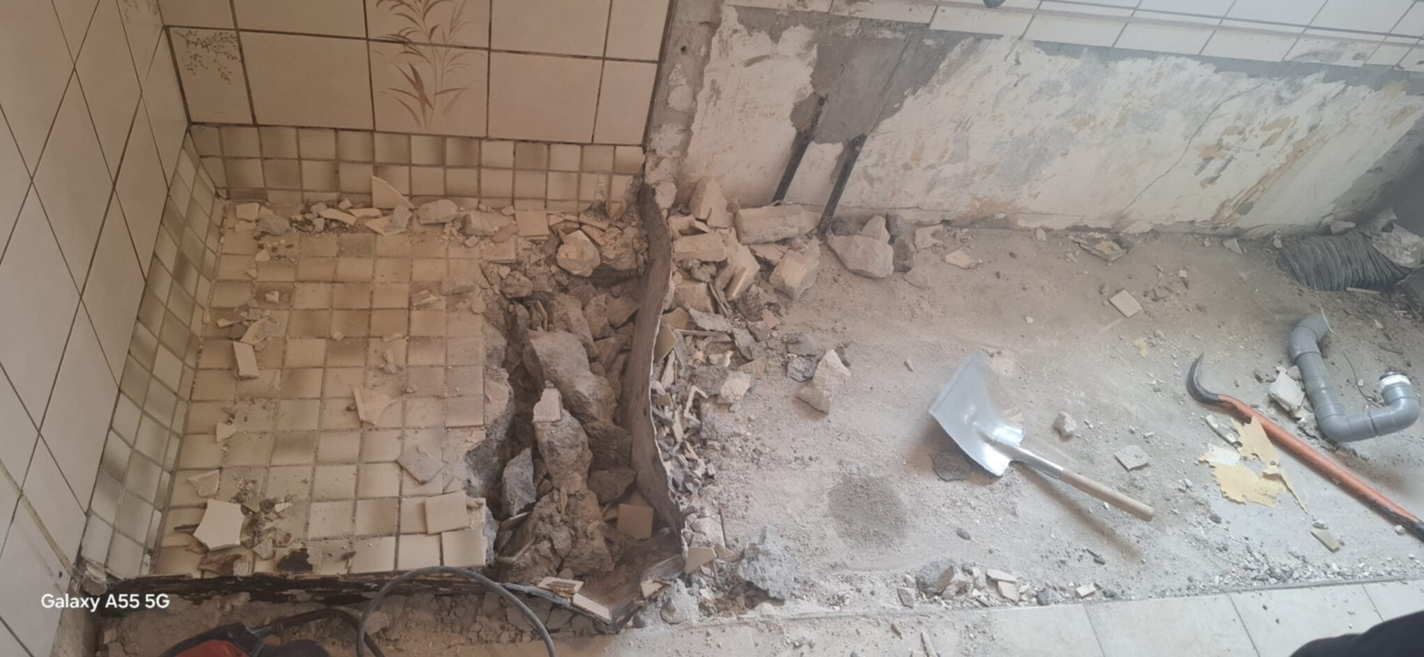 Sloopwerk badkamer met kapotte tegels en puin op de grond