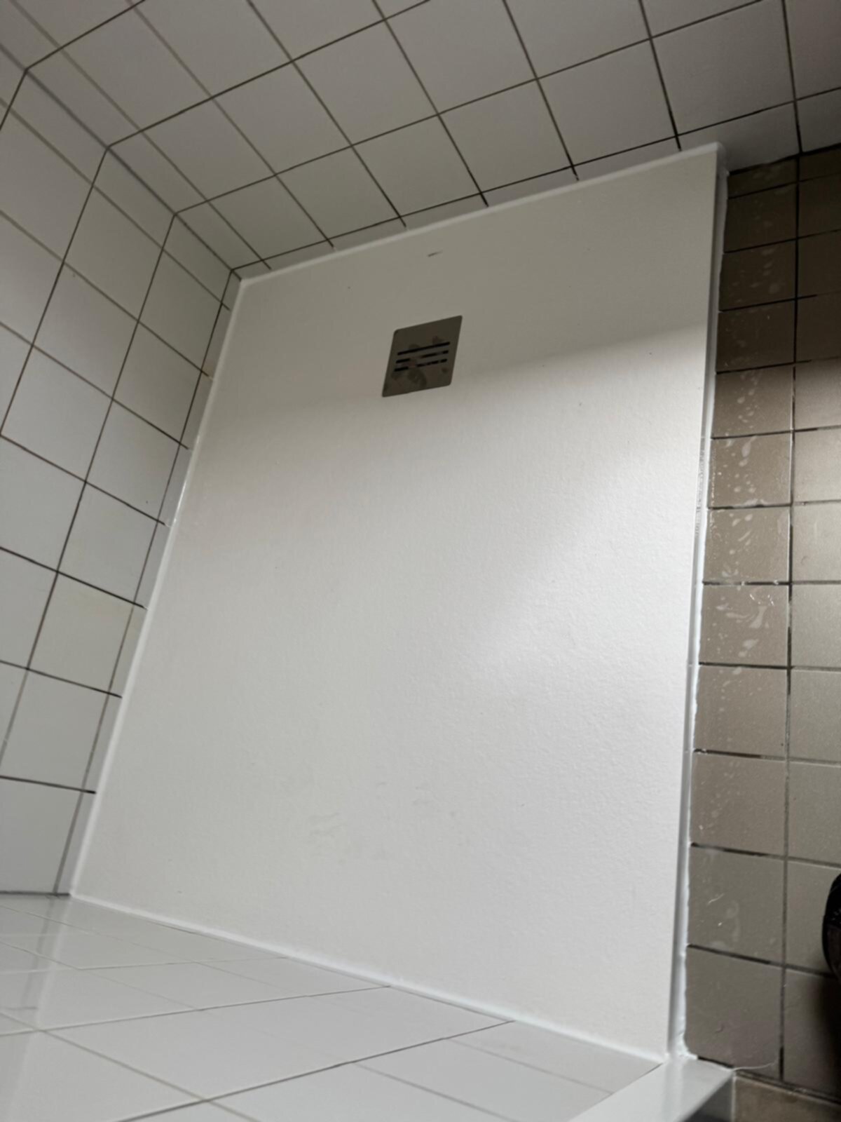 Wit betegelde badkamer met witte douchewand en grijs betegelde muur