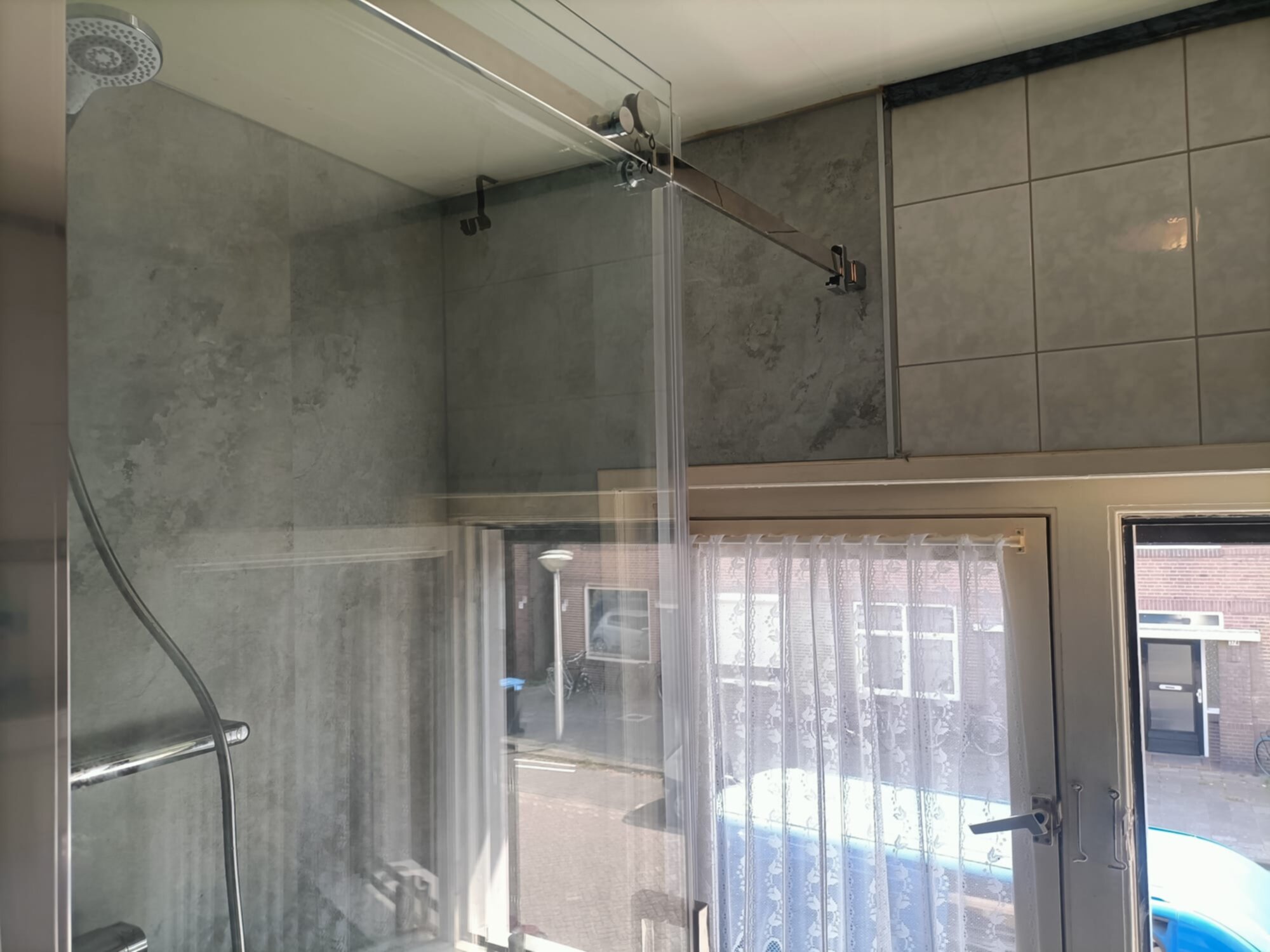Douche met glazen deur en grijs betegelde wanden