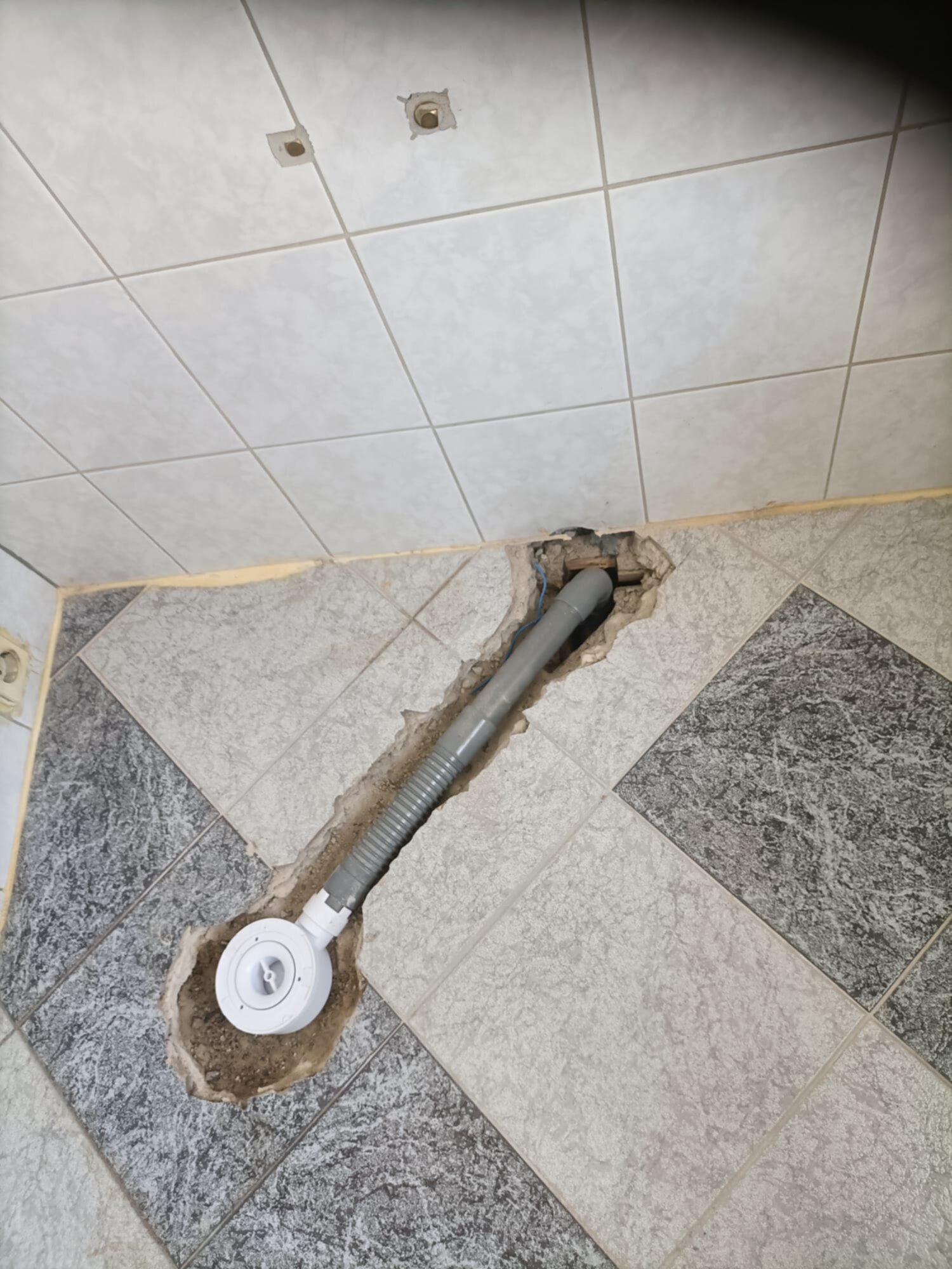 Sleuf in de badkamer vloer met blootgelegde leidingen en tegelwerk