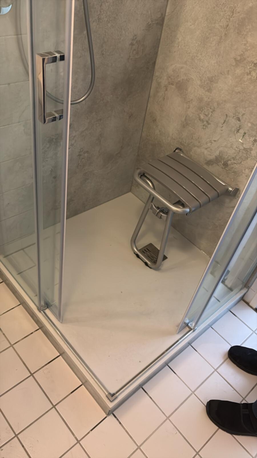 Douchecabine met glazen deur en zilveren douchestoel