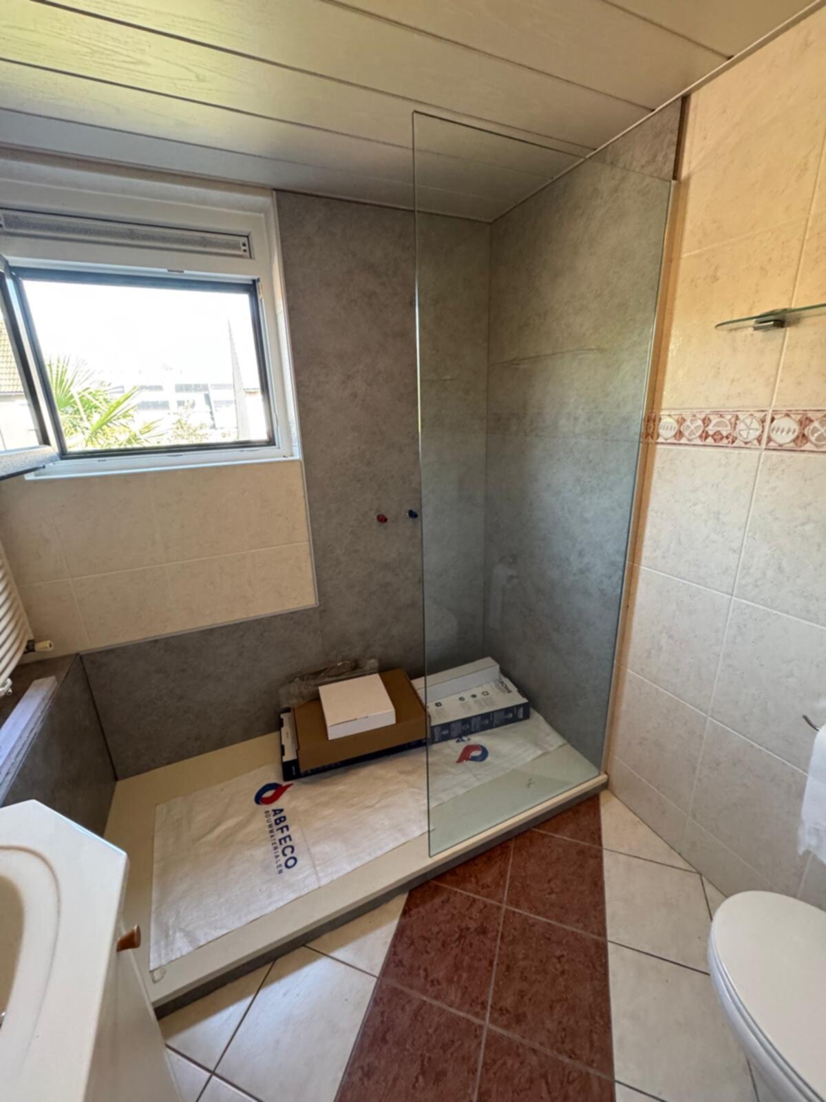 Douchehoek met glazen deur en betegelde wanden in beige en bruin