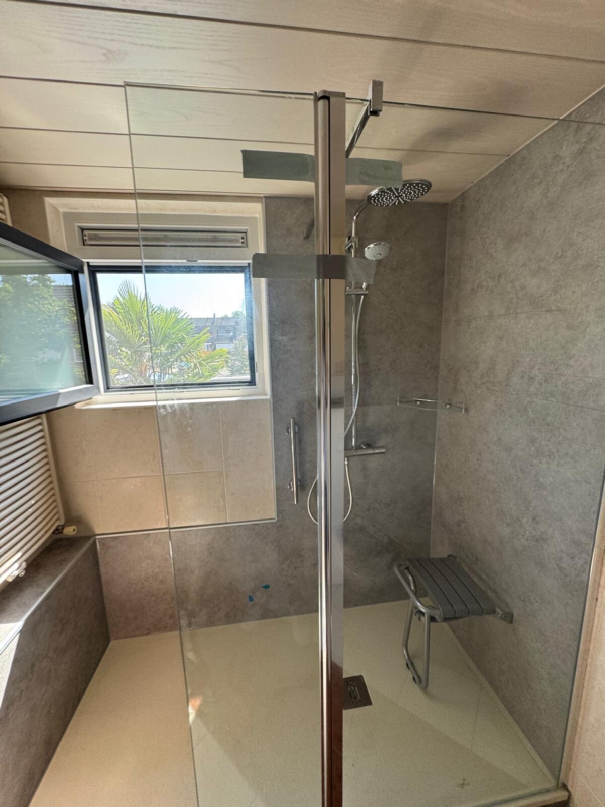 Douche met glazen deur en zilveren kraan, grijze en beige tegels