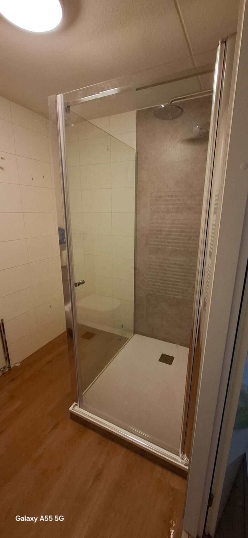 Douchecabine met glazen deur en wand, witte en grijze tegels, houten vloer