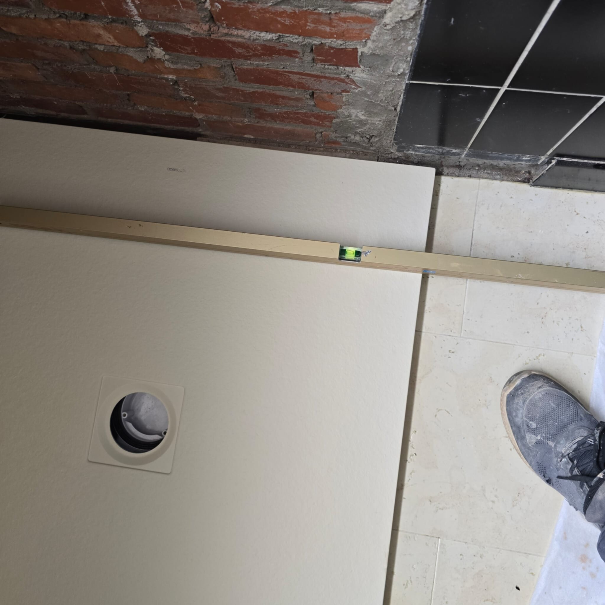 Wit betegelde badkamerwand met waterpas en schoen tijdens renovatie