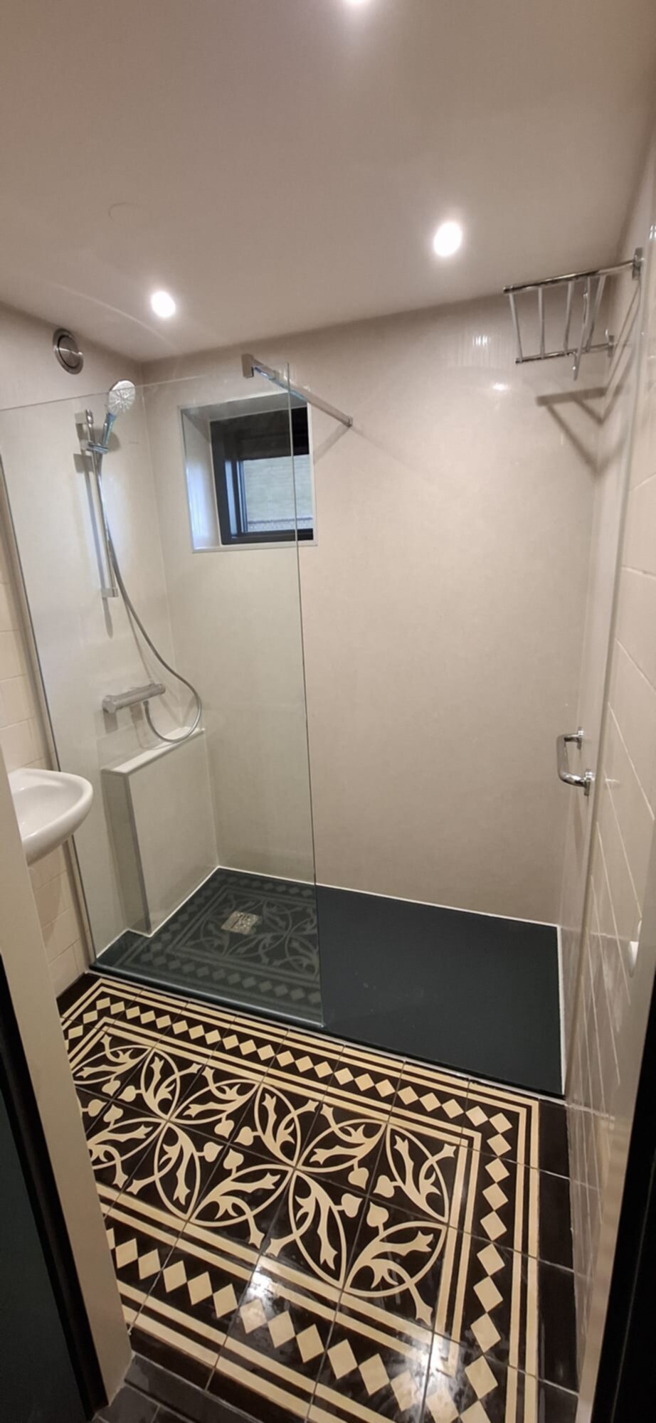 Douche met glazen wand, beige en bruine tegels en een vloer met een bloemmotief