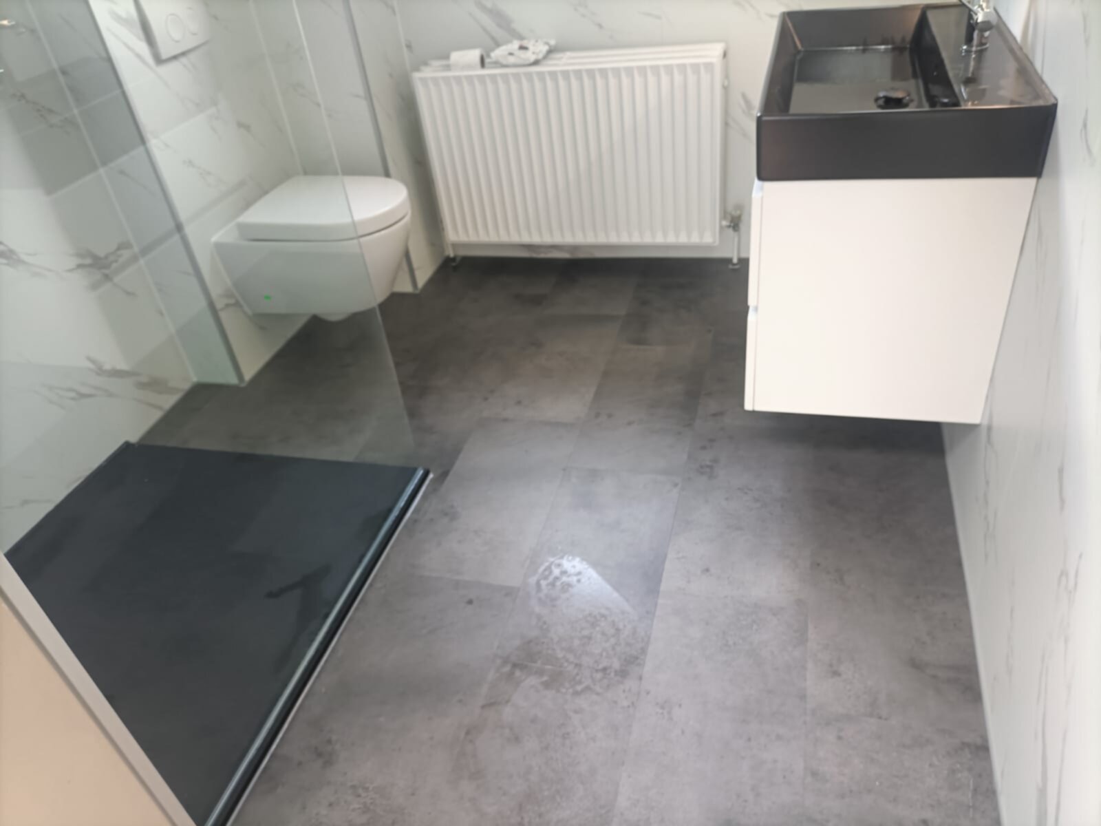 Moderne badkamer met witte en grijze marmerlook tegels, zwarte douchebak en wit toilet