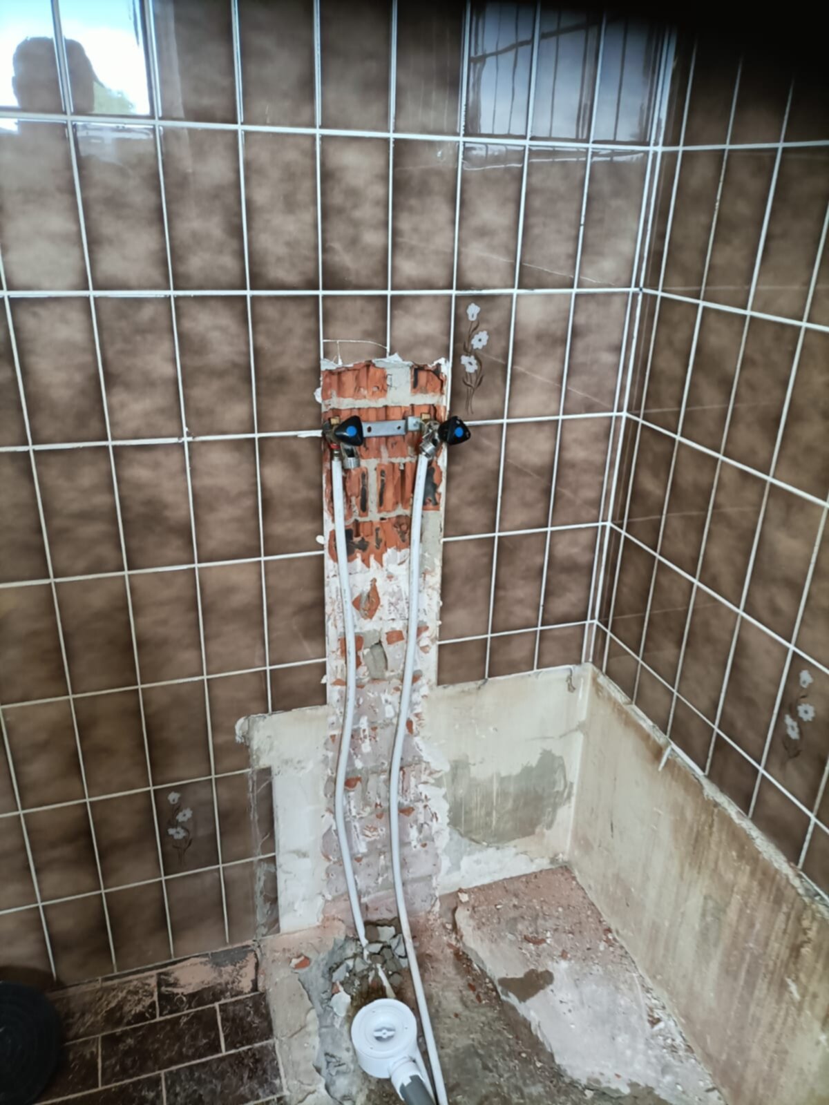 Slechte staat badkamer met kapotte tegelwand en open leidingen