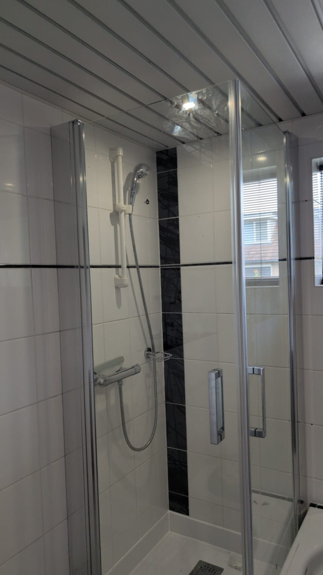 Douchecabine met glazen wand en deur, witte tegels met zwarte strook