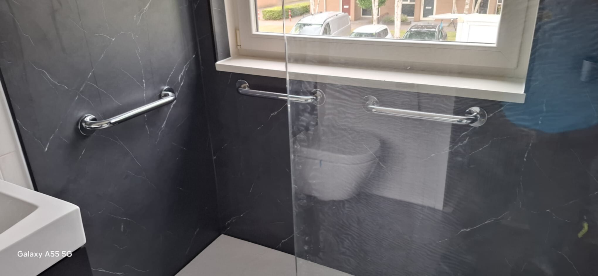 Badkamer met grijze marmeren tegels, glazen douchedeur en witte wastafel