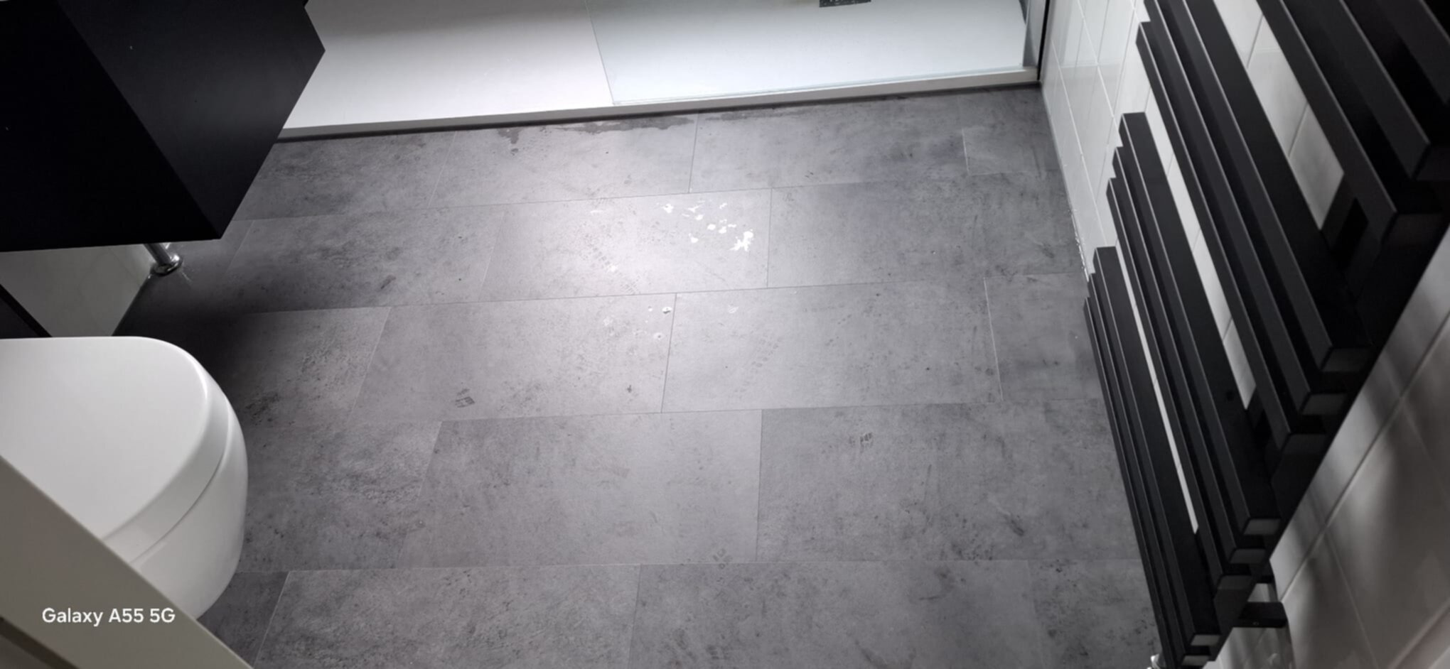 Grijze tegelvloer in moderne badkamer met witte toilet en zwarte radiator