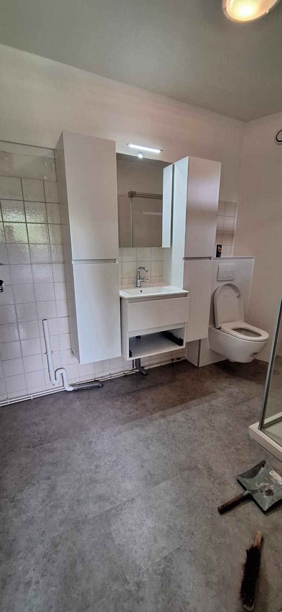 Slechte witte badkamer met betegelde muren en grijze vloer tijdens renovatie