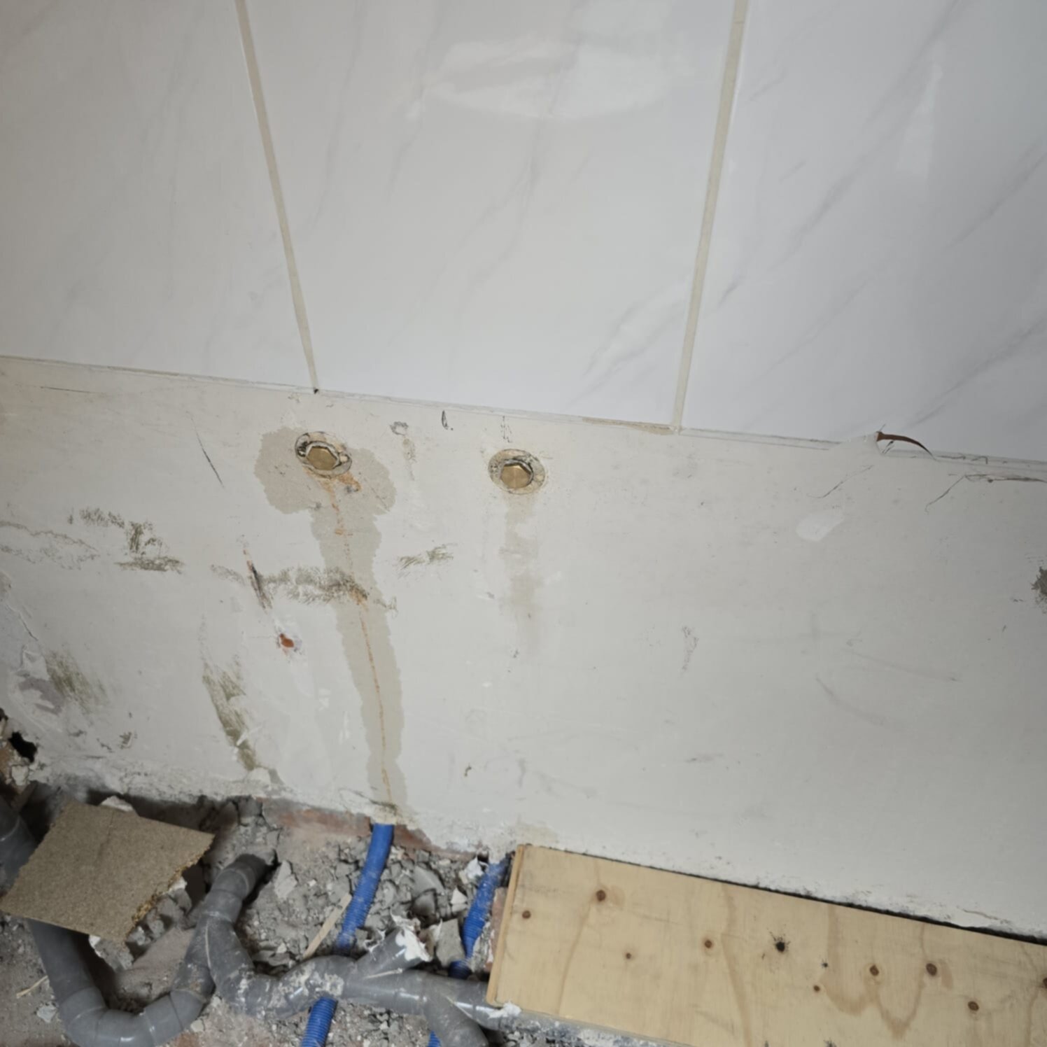 Sleuf in badkamerwand met blootgelegde leidingen en marmeren betegeling