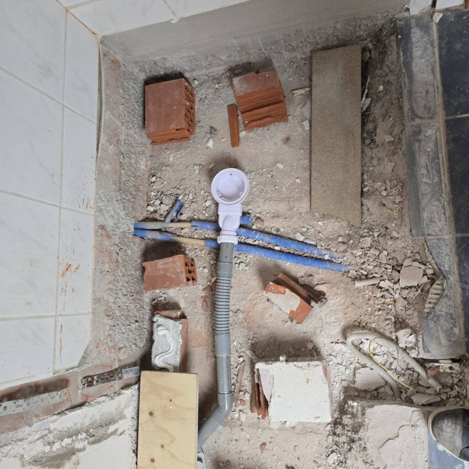 Sleuf in badkamer vloer met zichtbare leidingen en bouwmaterialen tijdens renovatie