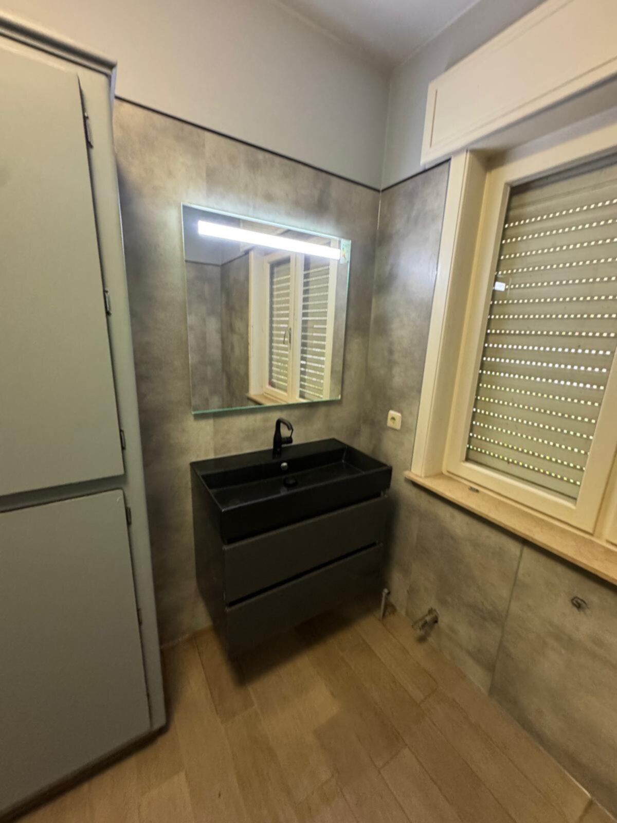 Moderne badkamer met grijze wanden, zwarte wastafel en spiegel met licht