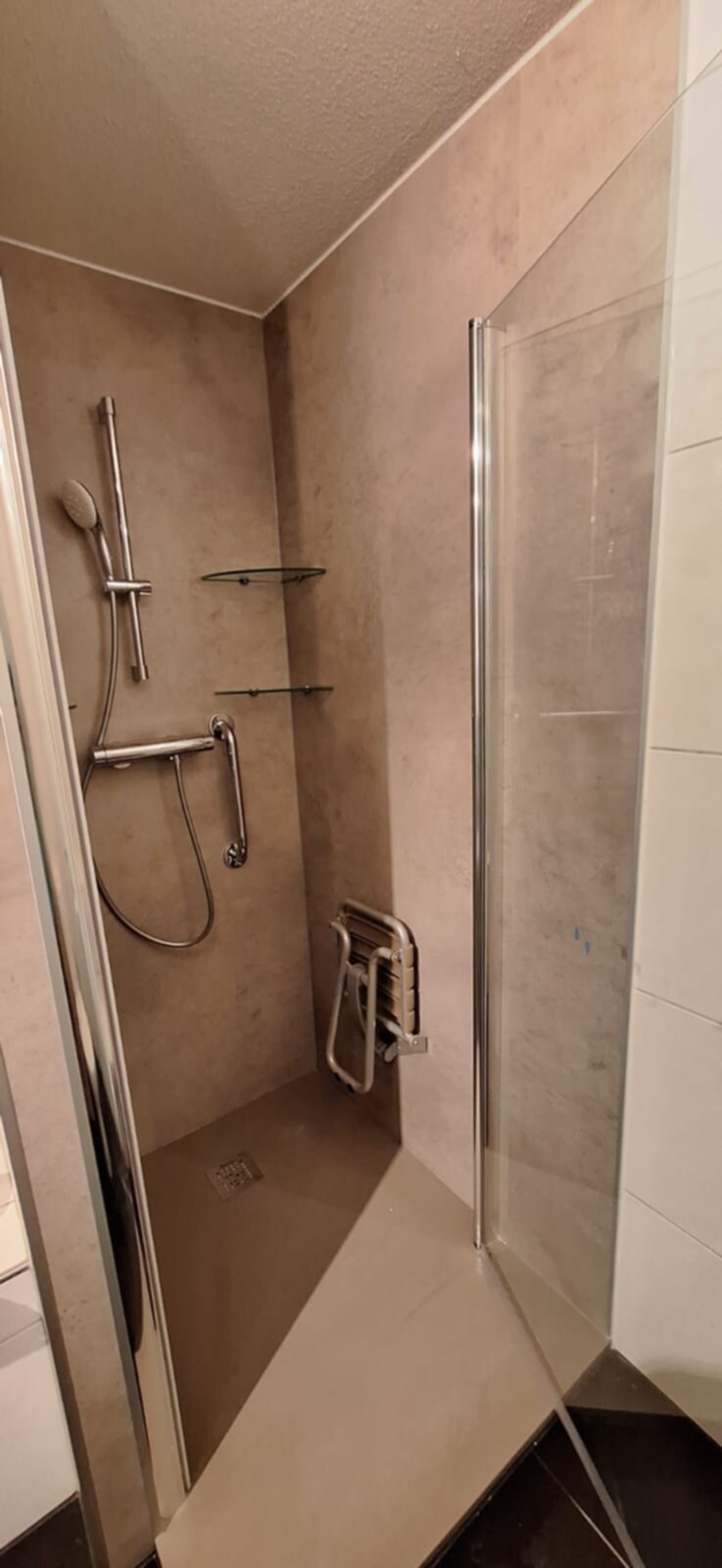 Douchecabine met glazen deur en beige betegeling, metalen douchekop en greep