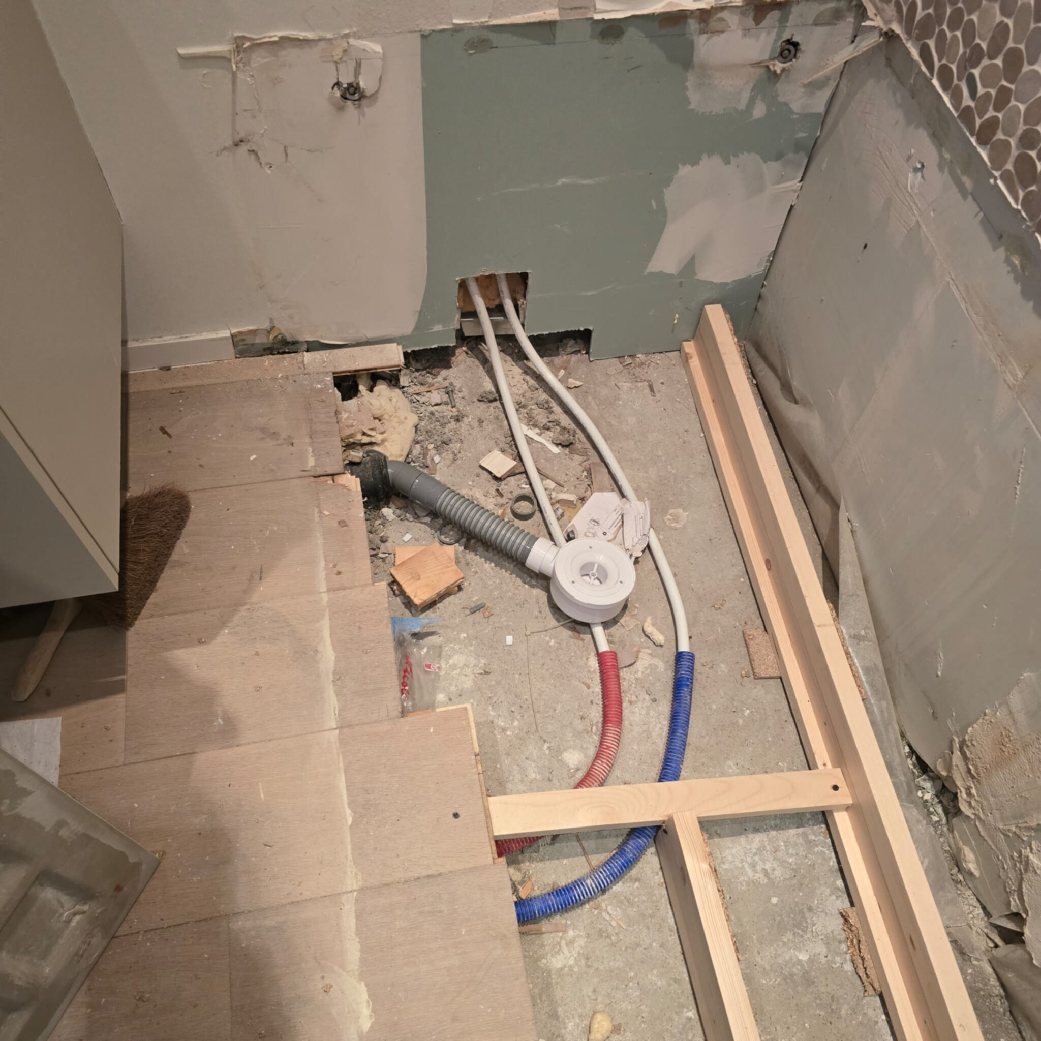 Sleuf in badkamer vloer met blootgelegde leidingen en houten constructie tijdens renovatie