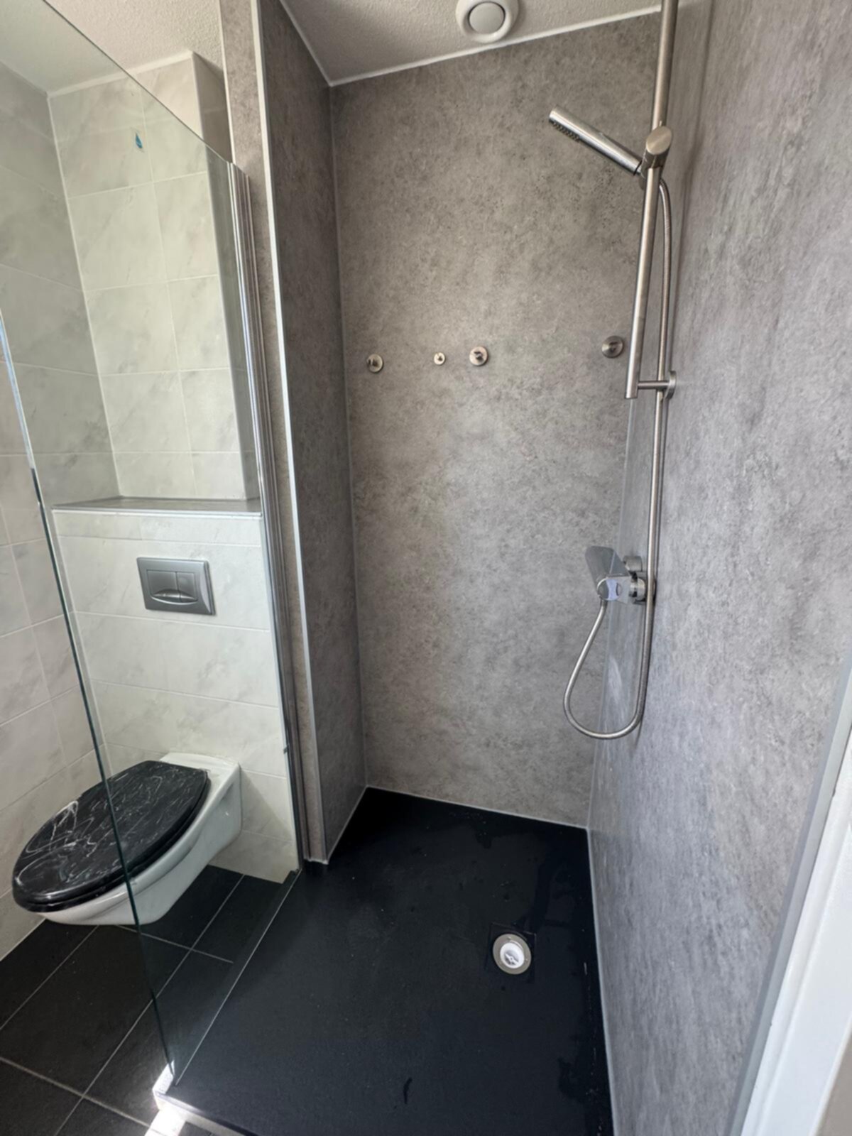 Moderne badkamer met grijze wanden, zwarte vloer en glazen douchecabine