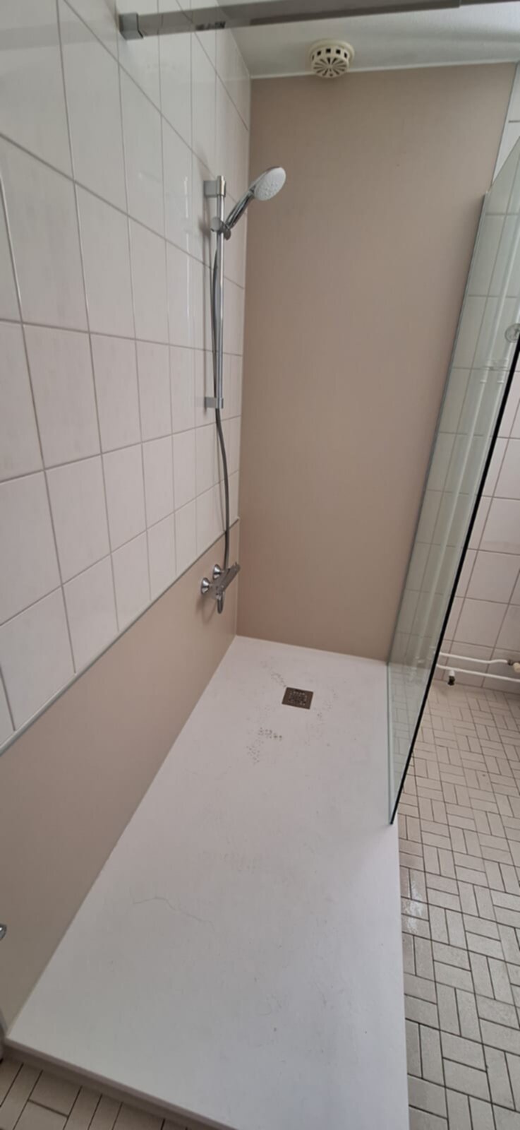 Douchecabine met witte tegelwand en beige muur, chroom douchekop en glaswand