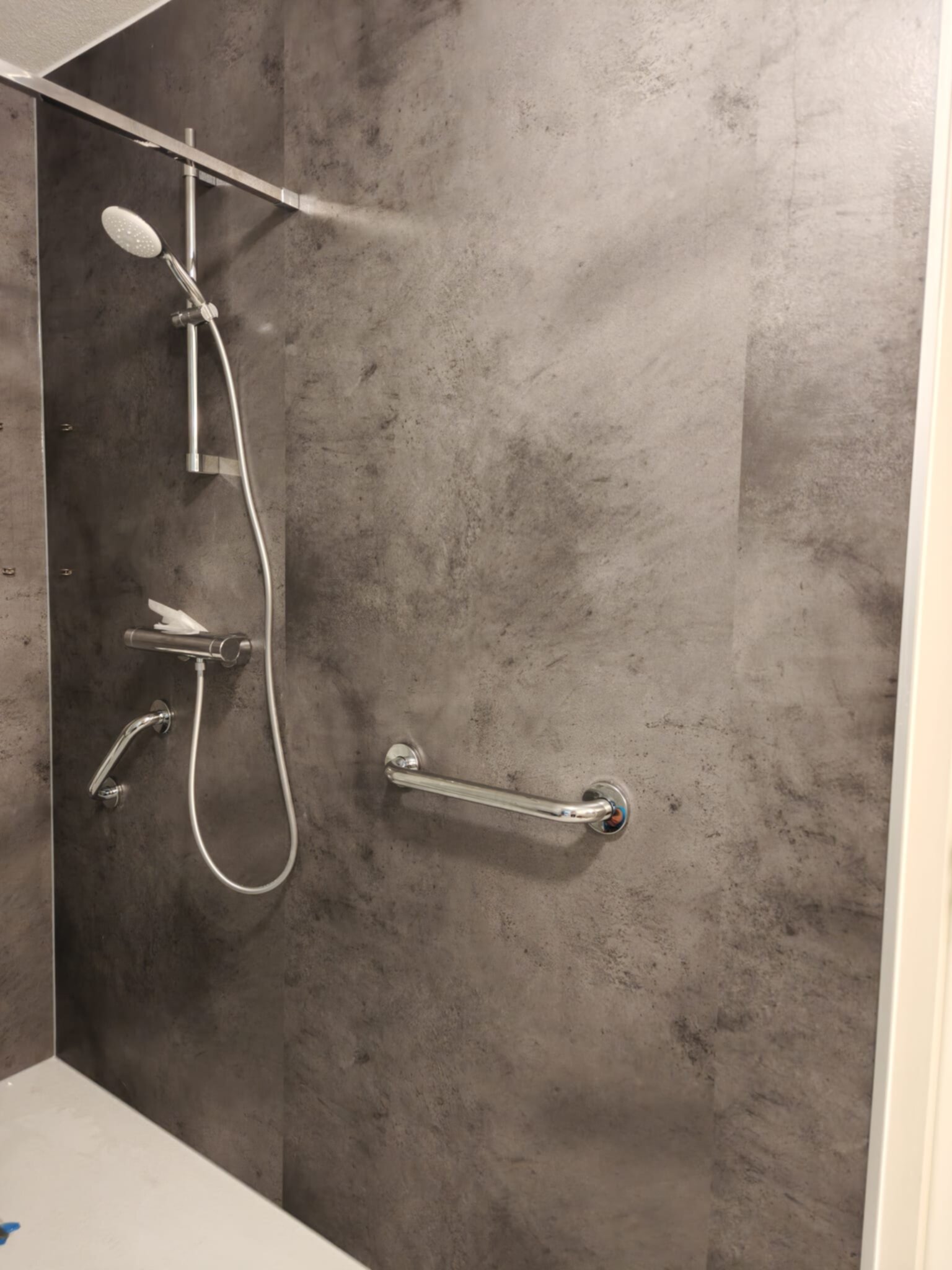 Douche met grijze wandtegels en een vaste douchekop en greep