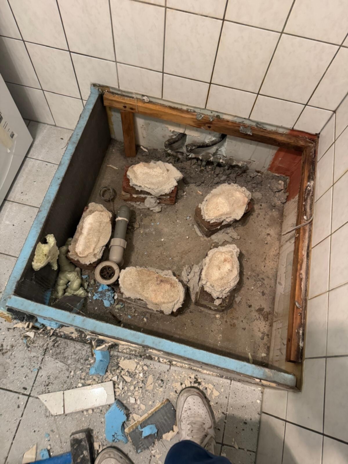 Sloop badkamer met betegelde wand en vloer, zicht op de kale beton en rioleringsbuizen