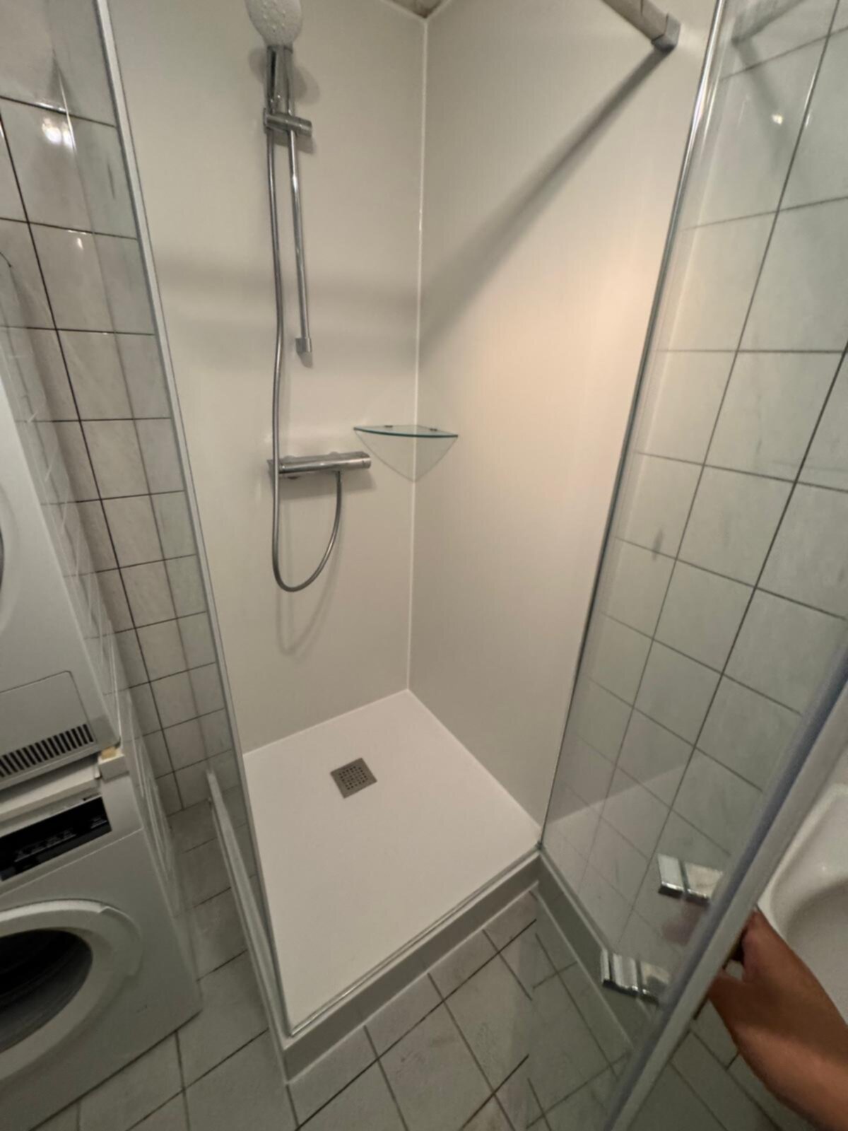 Douchecabine met witte wand en vloer, betegeld met grijze tegels en glazen deur