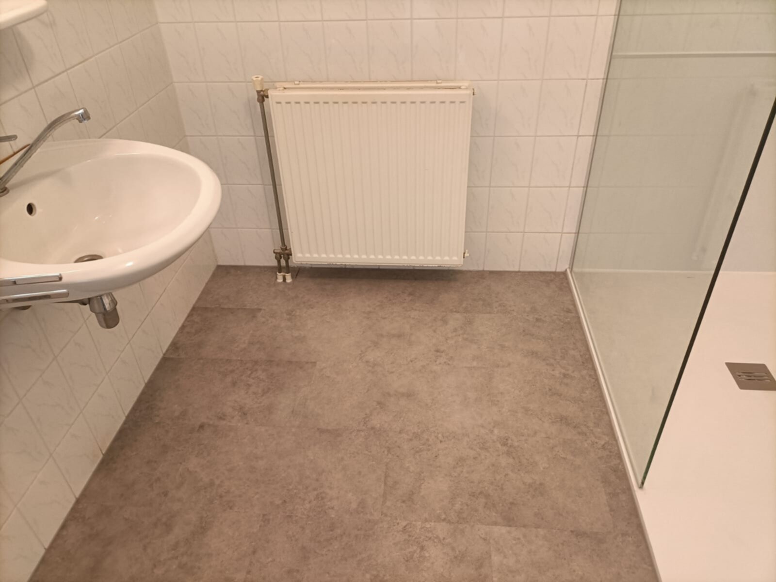 Wit betegelde badkamer met grijs betegelde vloer en witte wasbak